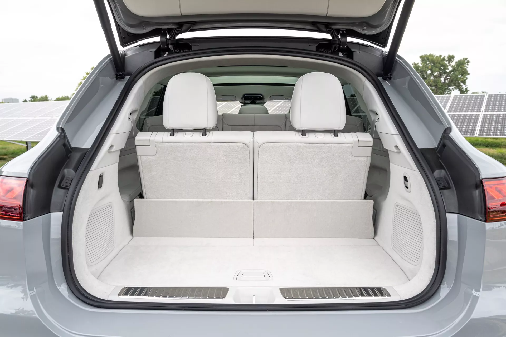Compartiment à bagages arrière du Mercedes EQS-SUV 2022 avec coffre ouvert, montrant un espace de rangement vide et des sièges arrière en position verticale. Revêtement intérieur de couleur claire, tapis assortis, compartiments de rangement latéraux et haut-parleurs arrière suggèrent un intérieur propre et luxueux. En mettant l'accent sur un vaste espace pour les bagages et objets personnels, l'image évoque un design moderne et fonctionnel.