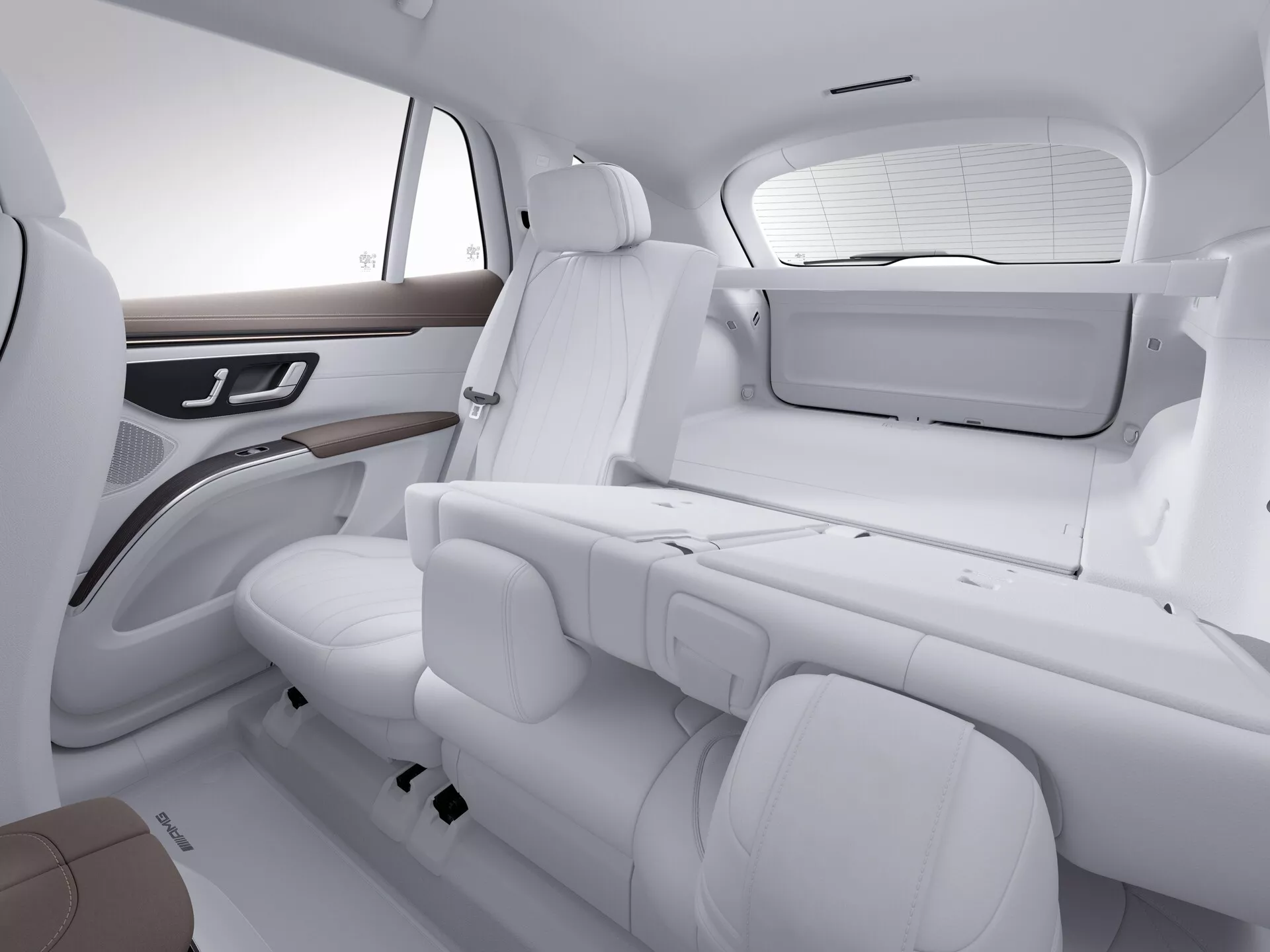 Vue en plongée de l'intérieur luxueux d'un Mercedes EQS-SUV 2022 montrant la zone des sièges arrière avec une sellerie en cuir blanc, des accents marron et des garnitures en bois. Comprend les sièges arrière, une partie du siège passager avant, le panneau de porte arrière avec commandes de fenêtre électrique et un petit écran à l'arrière du siège passager avant. L'éclairage brillant met en valeur le design épuré et minimaliste et l'état bien entretenu.