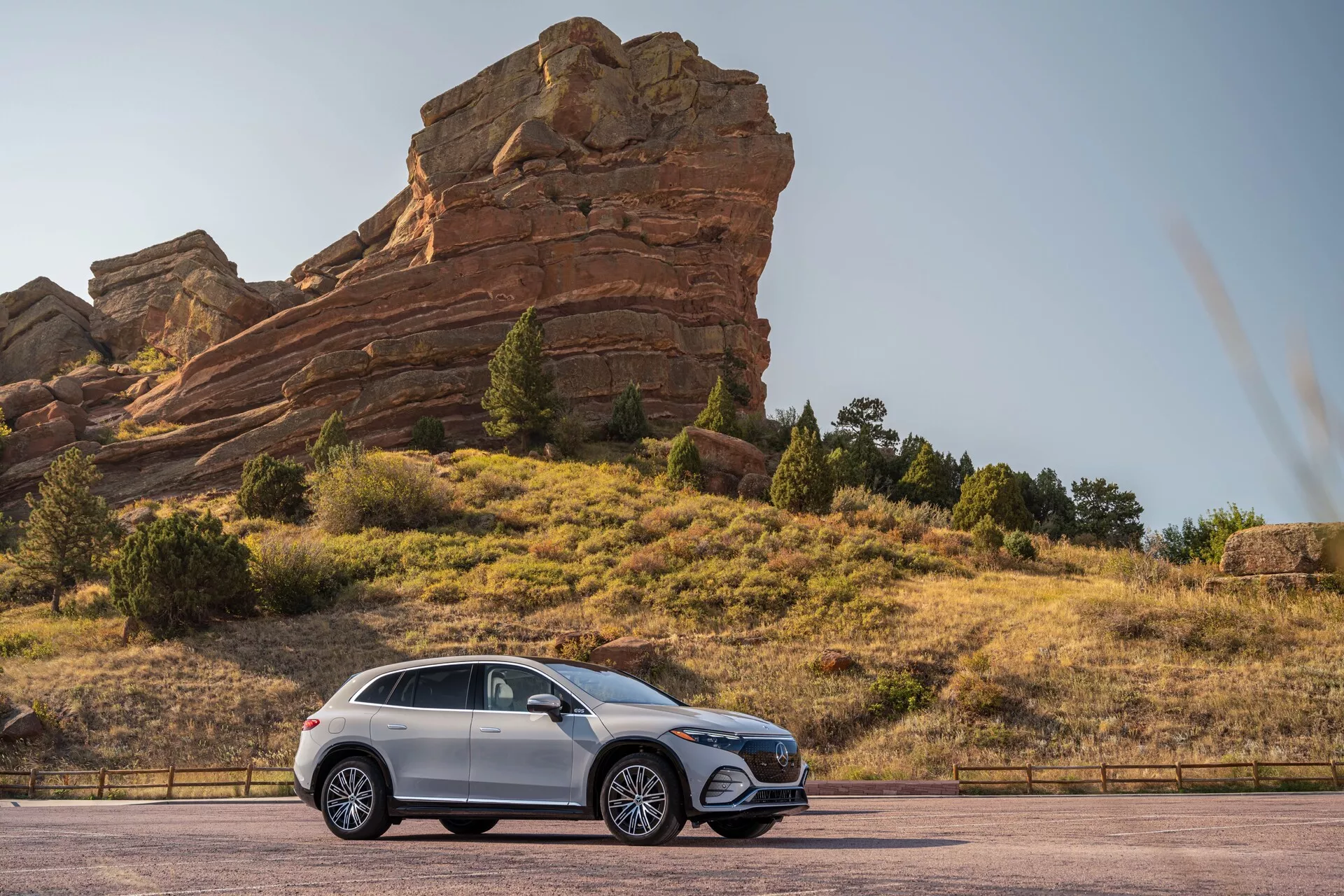 Vue de profil latéral d'un Mercedes EQS SUV 2022 garé sur une route pavée avec de grandes formations rocheuses en arrière-plan, accentuant sa garde au sol élevée, ses roues en alliage, ses lignes de design élégantes, ses vitres teintées et sa finition de peinture métallique.