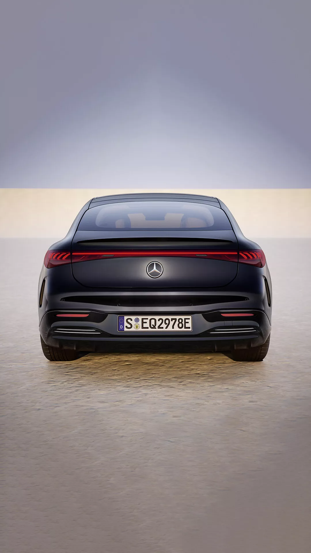Vue arrière du Mercedes-Benz EQS facelift 2024 présentant une bande lumineuse arrière LED, des capteurs de stationnement affleurants et une désignation de véhicule électrique sur un sol réfléchissant de showroom