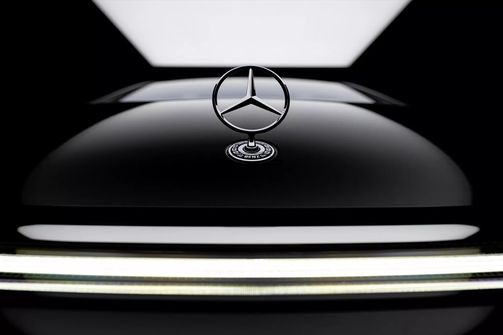 Vue rapprochée de la partie avant de la Mercedes-Benz EQS 2024 mettant en évidence le capot noir brillant et l'emblème emblématique étoilé, soulignant le design de luxe et la courbure élégante du véhicule.