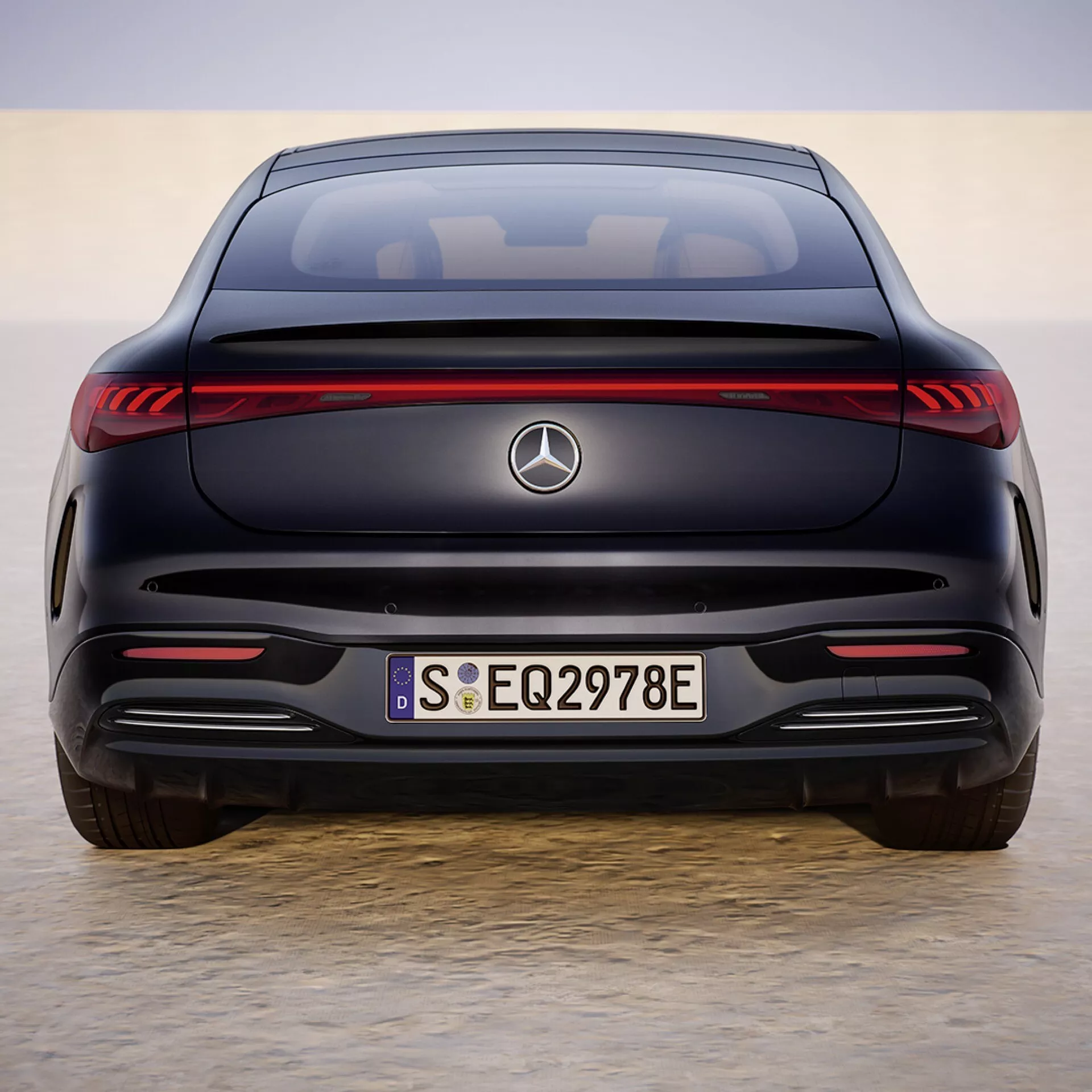 Vue arrière du Mercedes-Benz EQS 2024 présentant des feux arrière LED, emblème, badges EQ et 297E sur le coffre, pare-chocs arrière sans échappements, capteurs de stationnement et une silhouette de coupé indiquant les caractéristiques d'une berline électrique de luxe