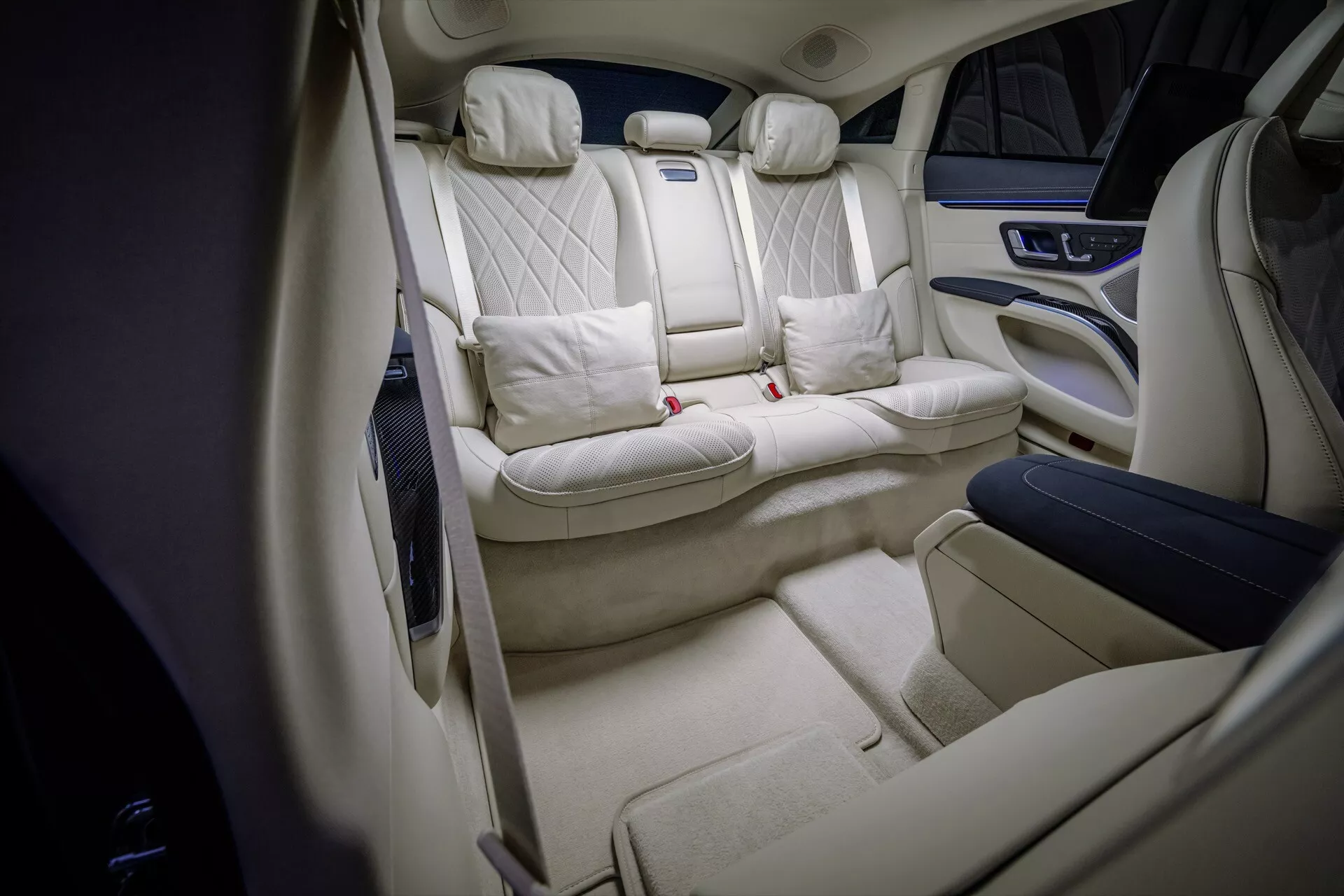 Vue intérieure du Mercedes-Benz EQS facelift 2024 montrant la cabine arrière luxueuse avec sièges à motif losange matelassé, sellerie en crème clair, console centrale haut de gamme, espace jambes étendu et éclairage d'ambiance