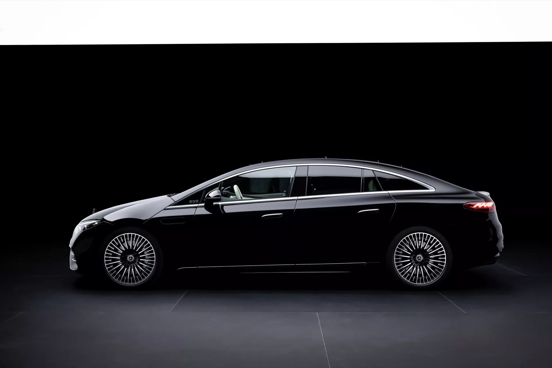 Vue de profil de la Mercedes-Benz EQS 2024 avec un lifting, montrant son empattement long, ses phares LED élégants et sa silhouette aérodynamique raffinée sur un fond sombre.