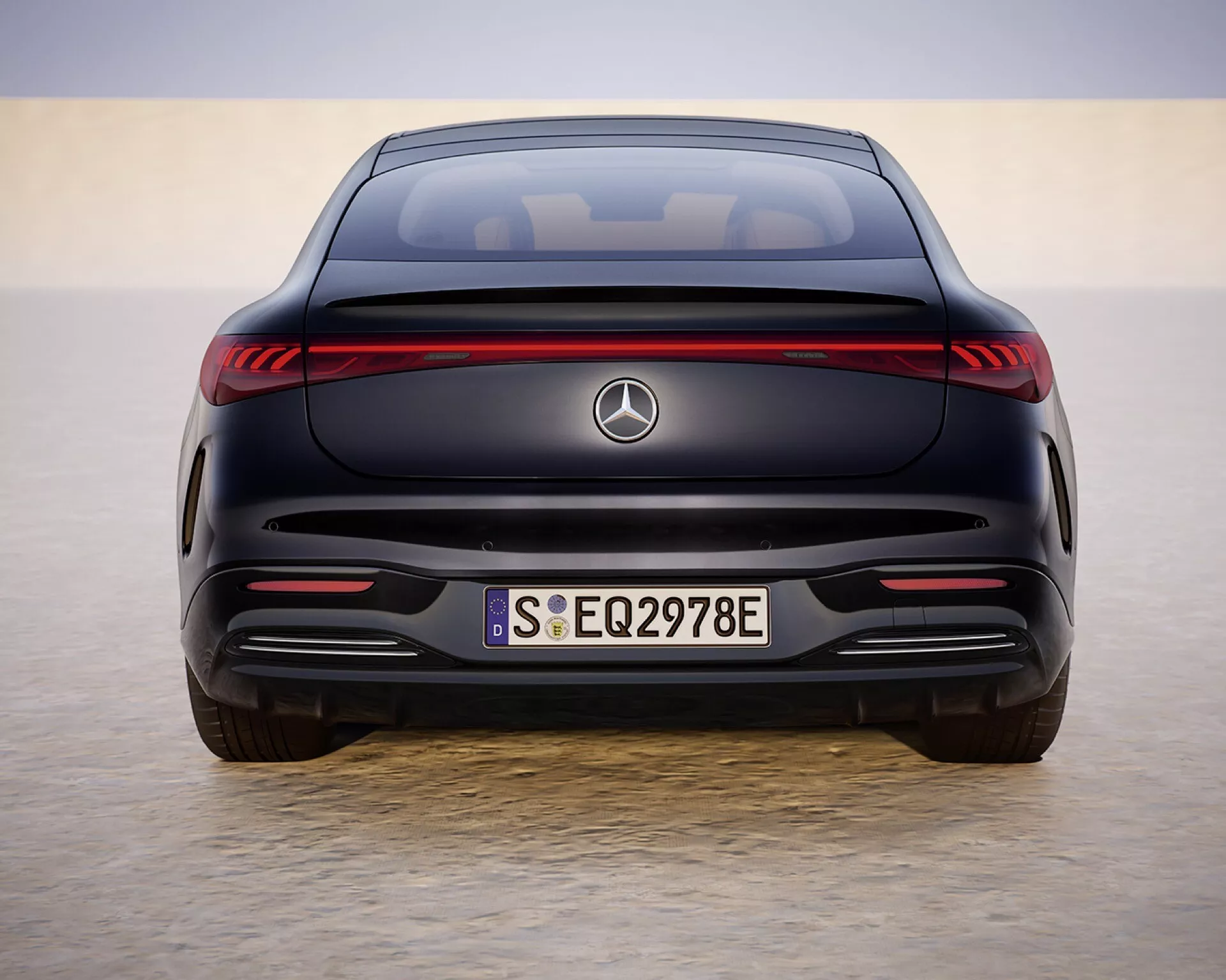 Vue arrière de la Mercedes-Benz EQS 297 facelift 2024 dans un cadre rappelant le désert, présentant des feux arrière LED, un badge EQ et un design de pare-choc sportif sous la lumière du jour