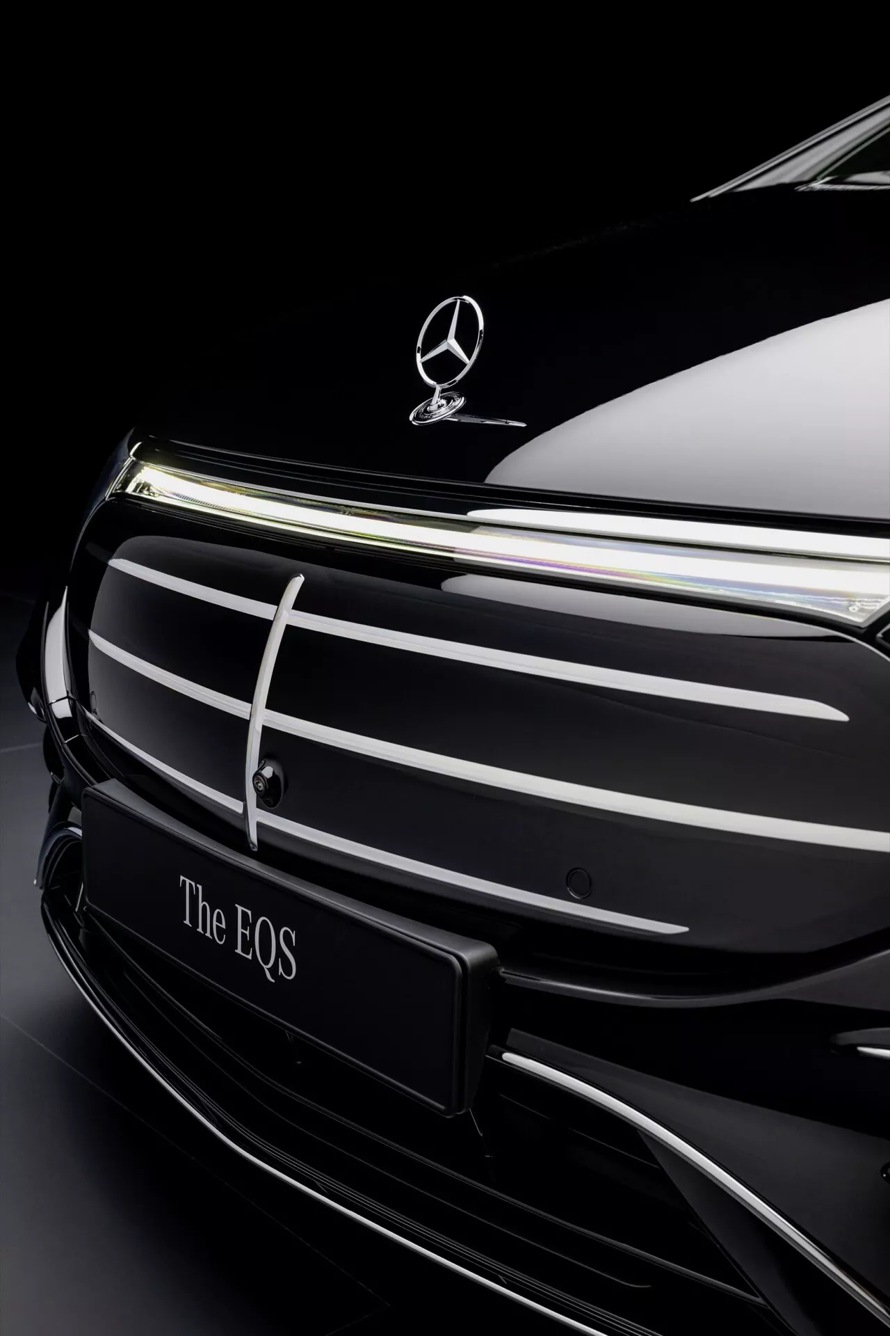 Gros plan sur l'avant du Mercedes-Benz EQS 2024 facelift avec emblème et grille chromée sur fond sombre soulignant le luxe et la conception de véhicules électriques