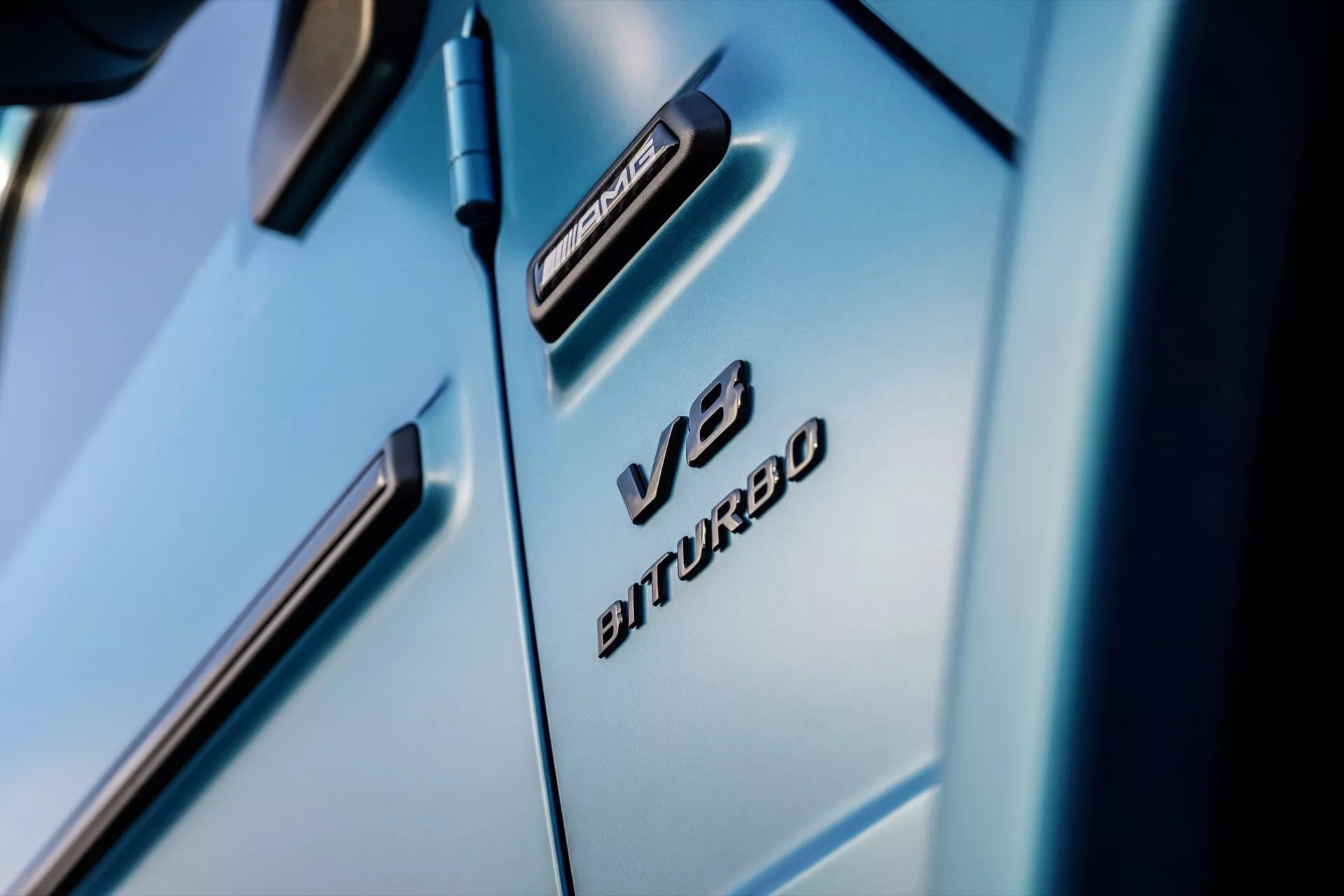 Gros plan sur l'aile avant de la Mercedes-Benz G-Klasse 2024 mettant en évidence les badges V8 BITURBO et 4MATIC, montrant des lignes de design de luxe et une finition bleu clair brillante