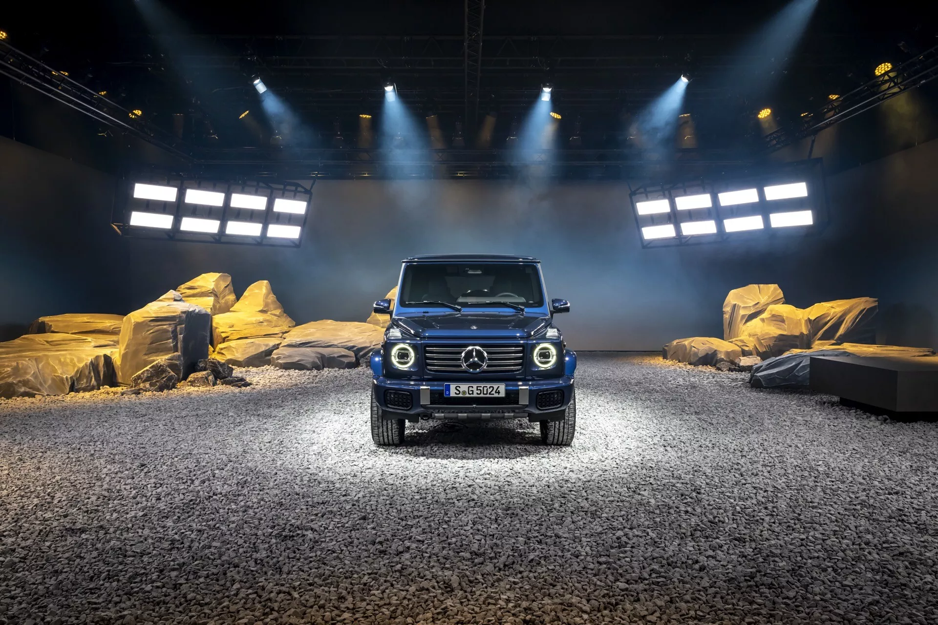 SUV Mercedes-Benz Classe G 2024 sur une scène extérieure simulée avec éclairage par projecteurs, montrant la grille avant, les phares ronds et un design robuste adapté aux conditions tout-terrain