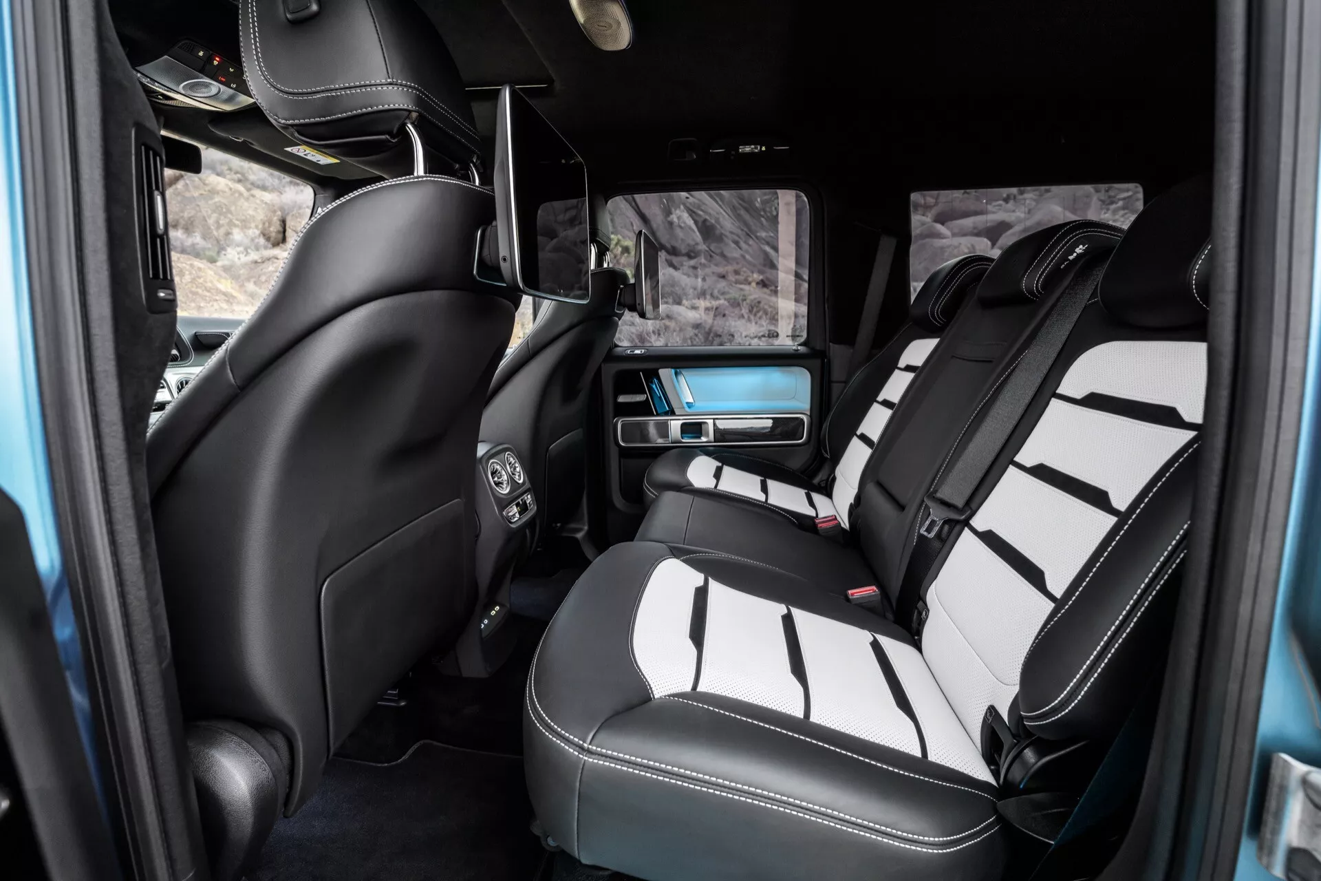 Intérieur de la Mercedes-Benz G-Klasse 2024 mettant en avant le compartiment passagers arrière de luxe, montrant des sièges en cuir bicolores, console centrale, contrôle climatique, système de divertissement et détails de finition haut de gamme