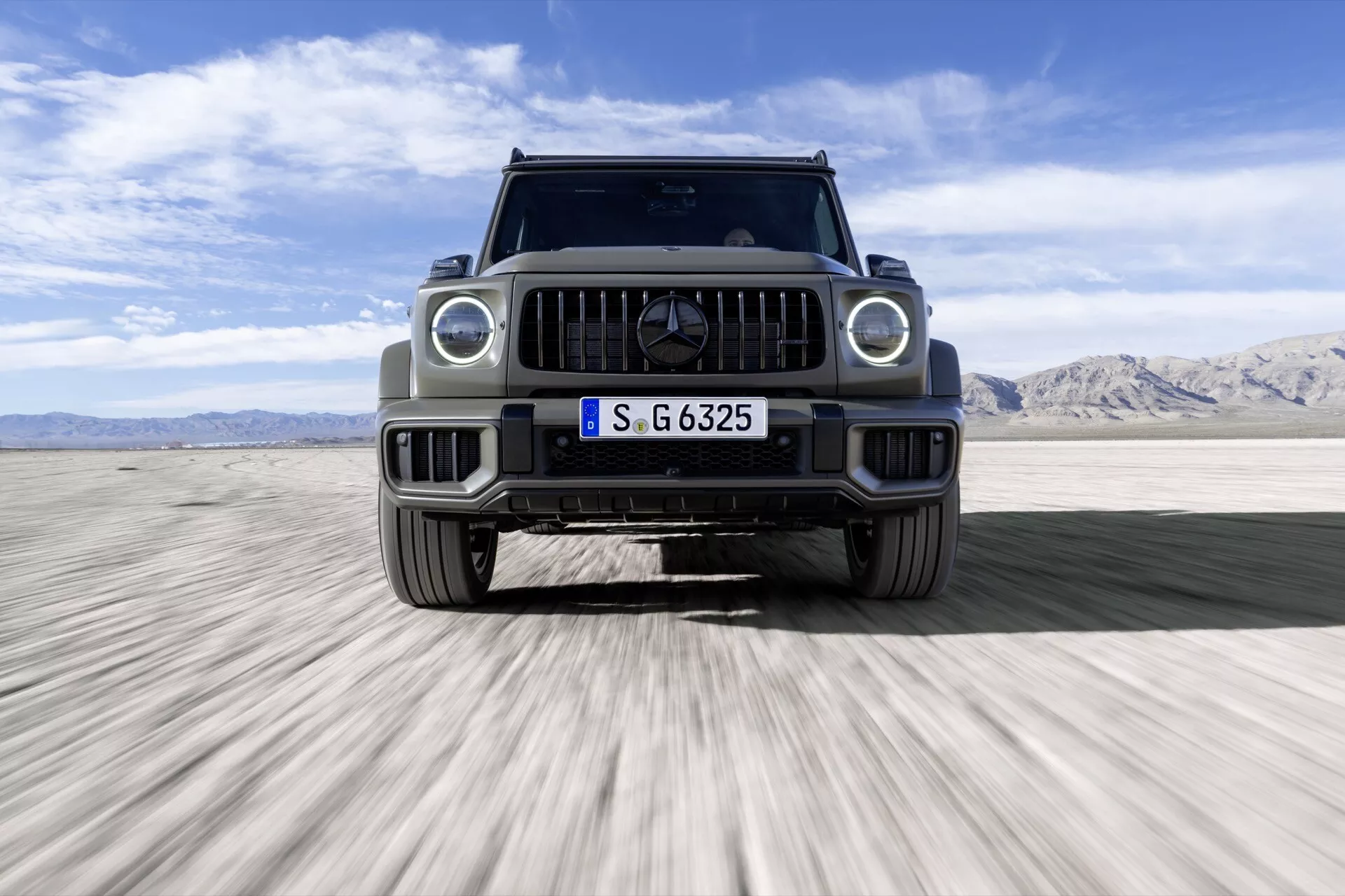 SUV de luxe Mercedes-Benz Classe G (G 465) de 2024, vue de face sur un désert, montrant des phares LED, calandre distinctive avec emblème et capacités tout-terrain.