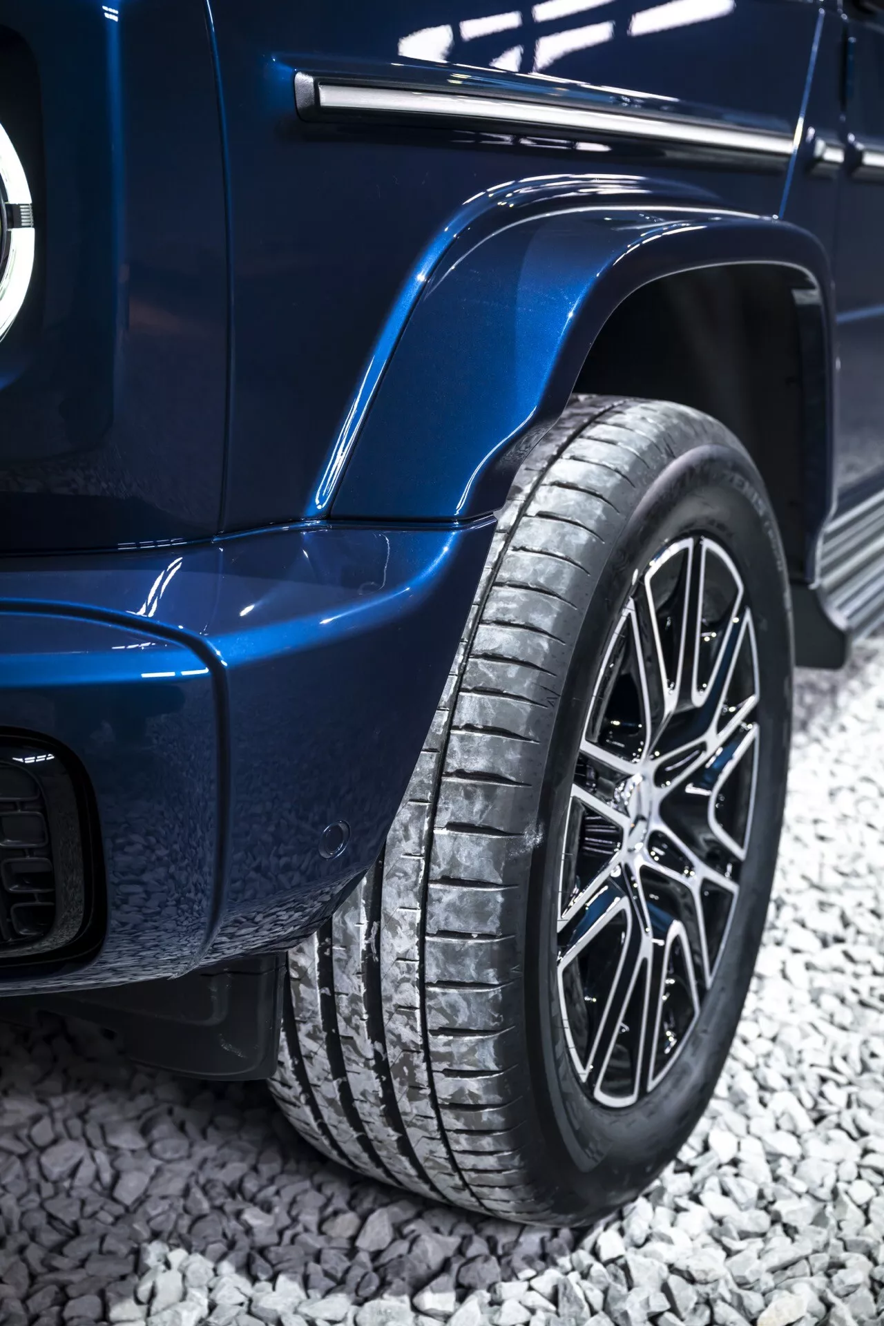 Gros plan sur la roue arrière et la carrosserie d'une Mercedes-Benz Classe G 2024 en bleu, avec une roue en alliage à multiples branches, un motif de bande de roulement prononcé et des ailes élargies suggérant des capacités haut de gamme ou tout-terrain
