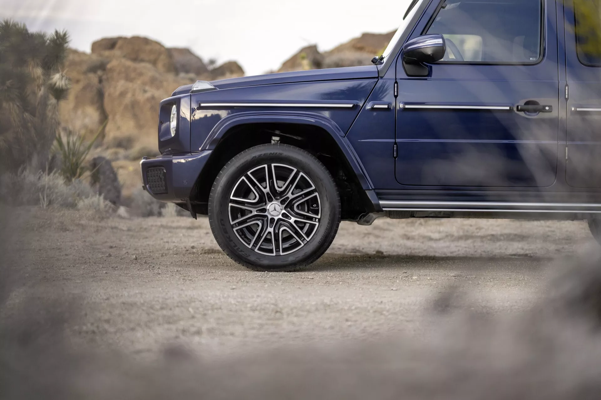 Gros plan sur la roue avant côté conducteur et l'aile d'une Mercedes-Benz G-Klasse 2024 en bleu foncé, présentant des roues en alliage de luxe et un profil latéral suggérant des capacités tout-terrain