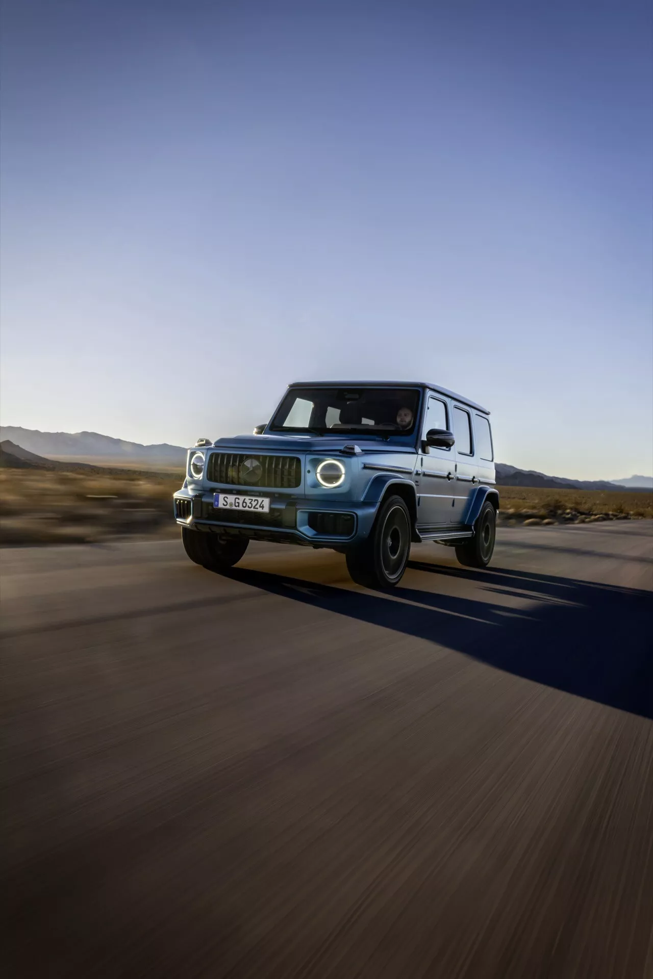 Mercedes-Benz G-Klasse 2024 en mouvement, présentant son design et ses caractéristiques de luxe depuis un angle avant et latéral bas, mettant en lumière les phares LED, la grille avant, les roues en alliage, et suggérant ses capacités à grande vitesse et son potentiel tout-terrain dans un décor désertique.