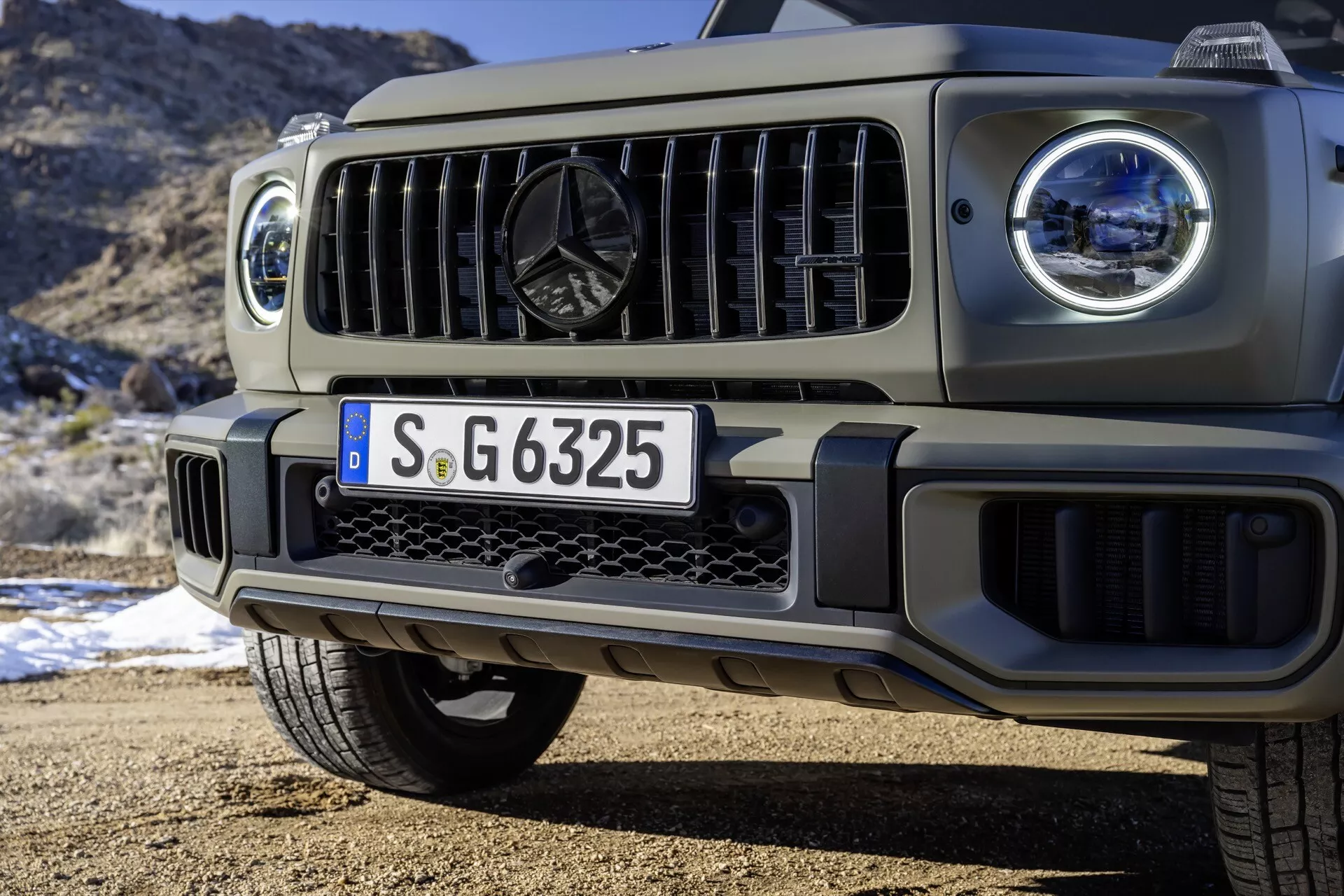 Vue rapprochée de l'avant du SUV Mercedes-Benz G-Class 2024, mettant en lumière les phares LED, la grille et la conception du pare-chocs avant sur fond naturel