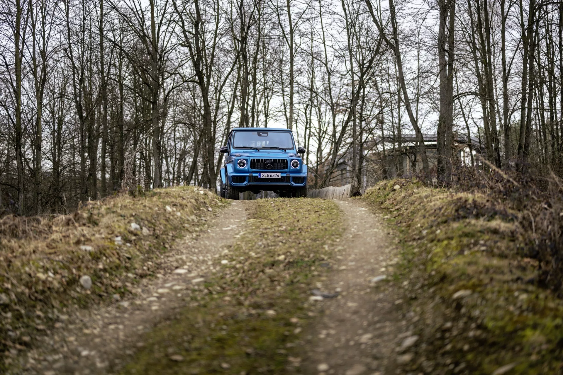 SUV bleu Mercedes-Benz G-Klasse 465 de 2024 sur chemin de terre dans une zone boisée présentant calandre avant, phares LED et capacité tout-terrain
