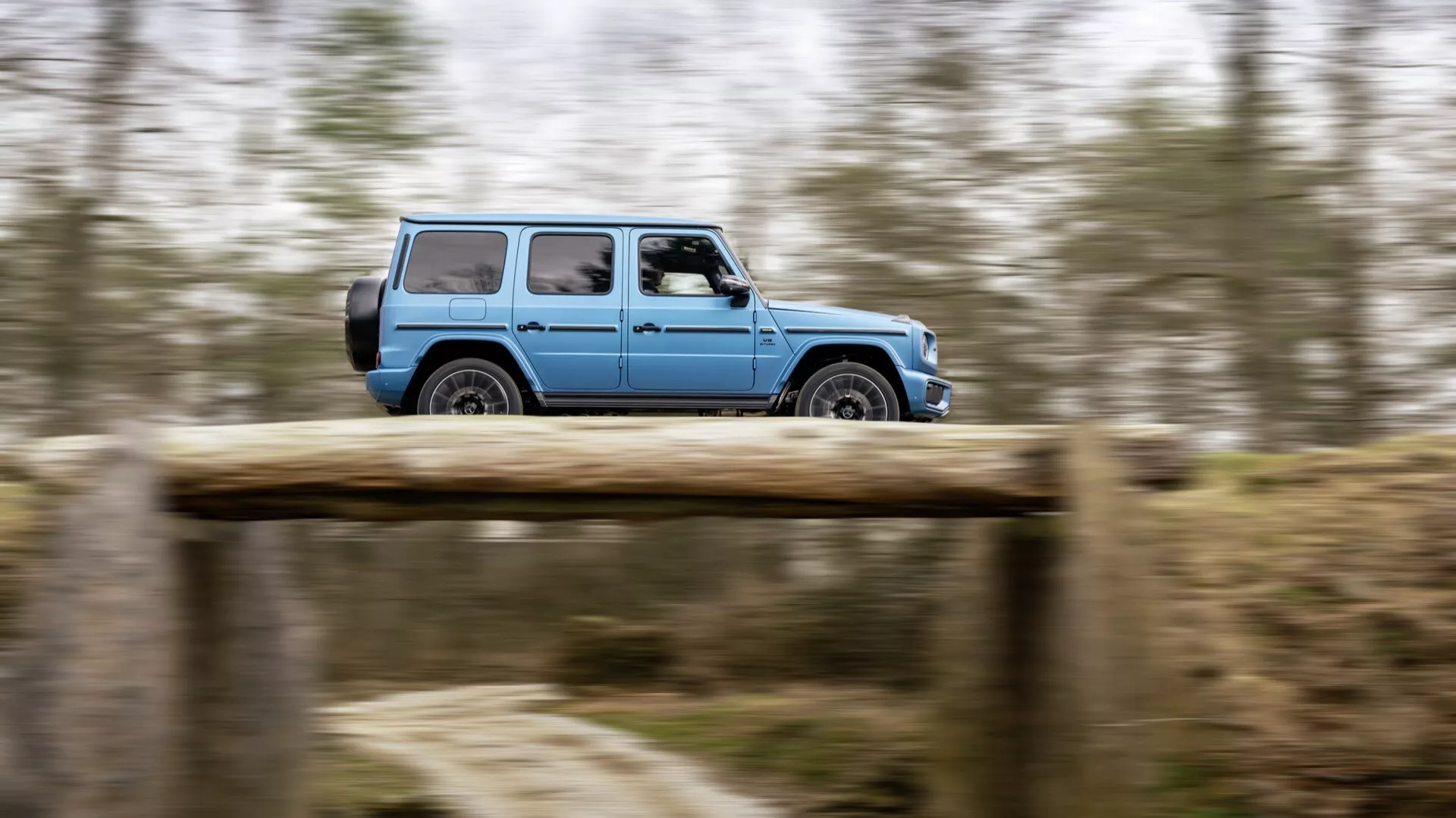 Mercedes-Benz G-Klasse (Classe G) 465 de 2024 se déplaçant sur une route de terre, capturée avec la technique de filé pour souligner le mouvement, affichant vue complète du profil mettant en évidence la conception tout-terrain et les roues en alliage.