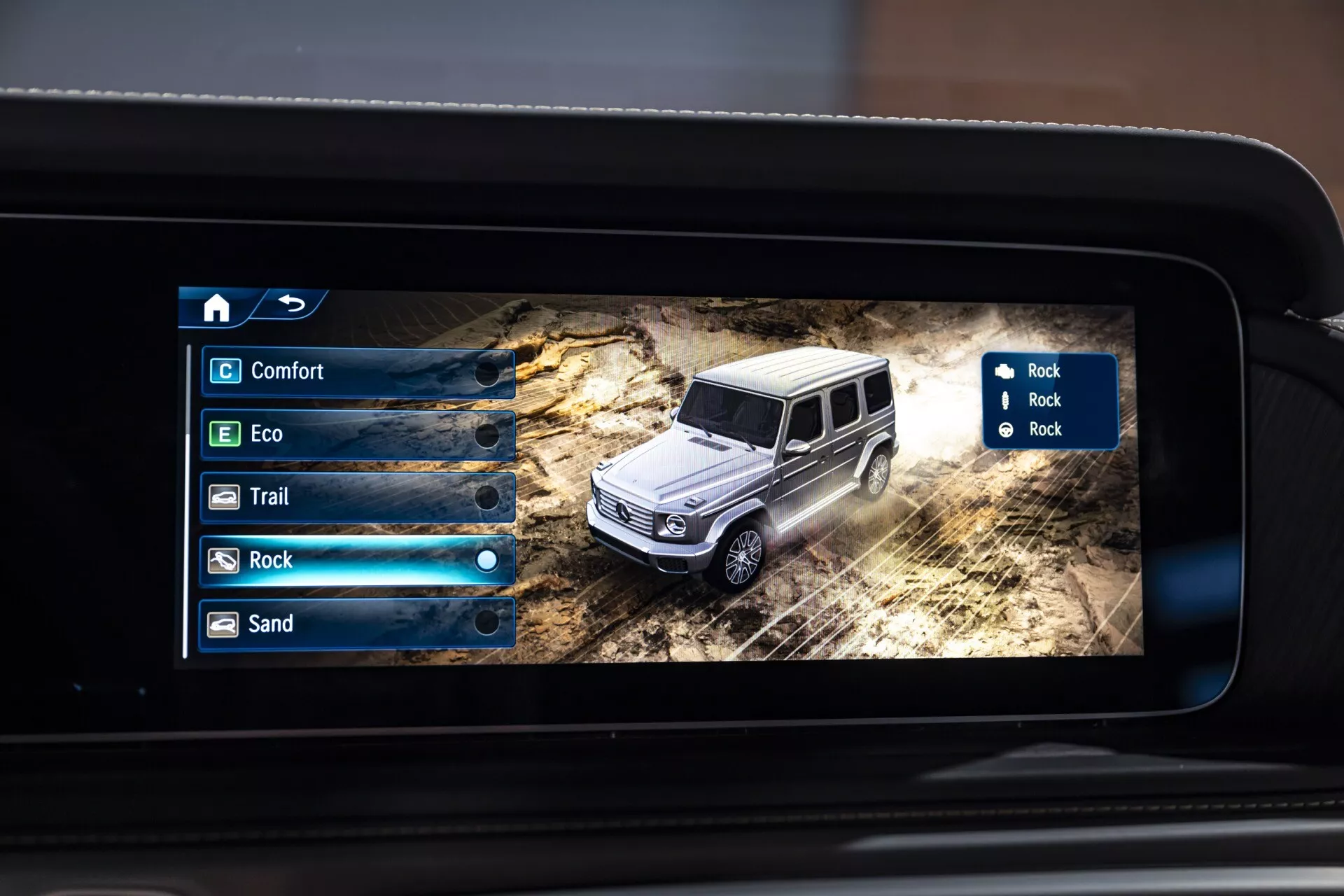 Gros plan d'un écran numérique à l'intérieur d'une Mercedes-Benz Classe G 2024 affichant un modèle 3D du SUV dans un environnement tout-terrain avec options de modes de terrain sur l'écran