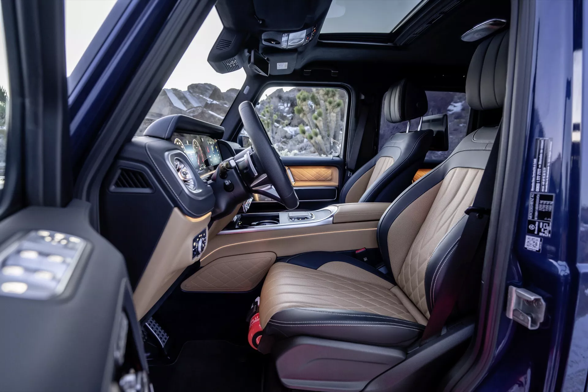 Vue intérieure de la Mercedes-Benz Classe G 2024 montrant les sièges avant et arrière en cuir avec accents de bois, l'infodivertissement et le toit ouvrant depuis un angle surélevé