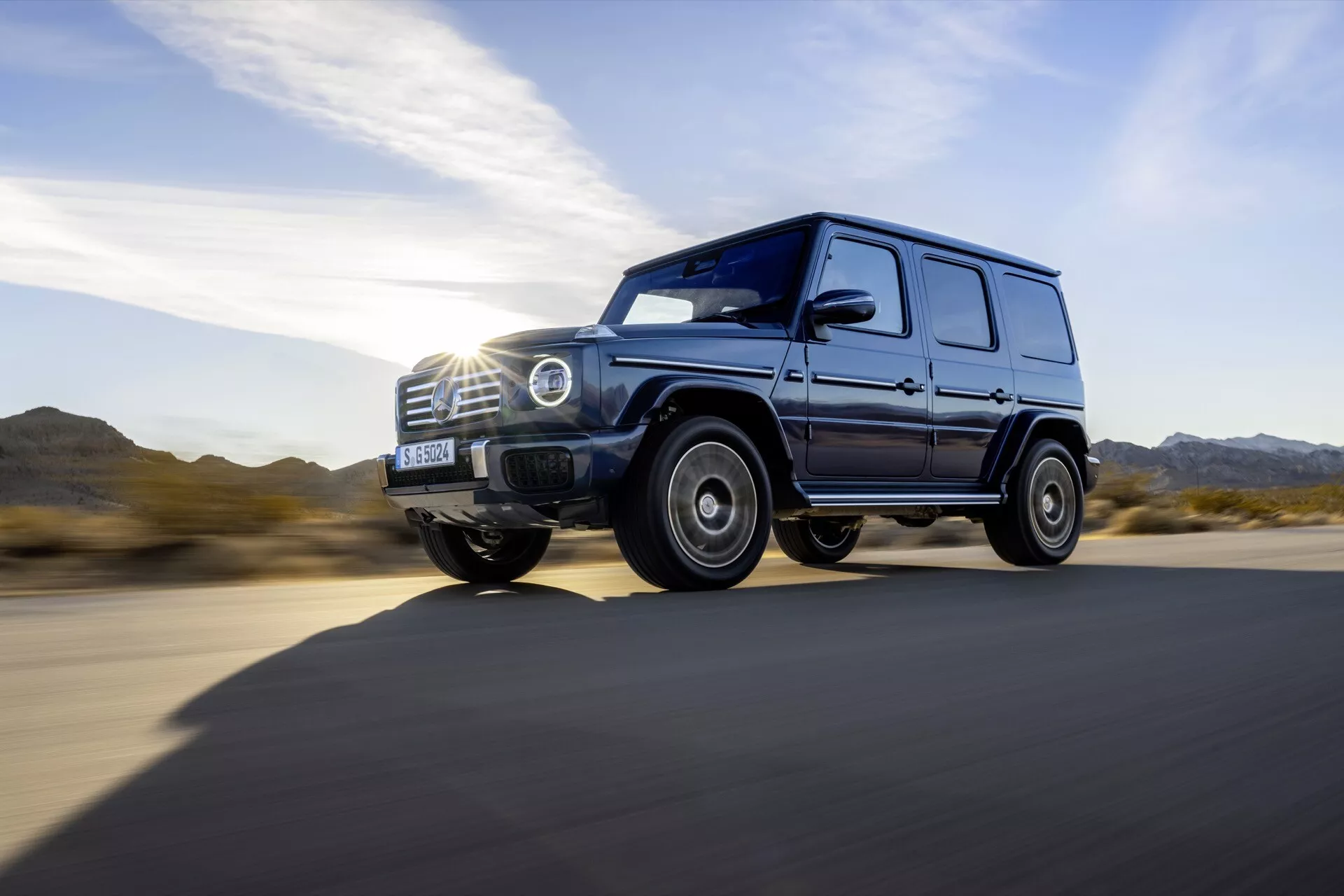 SUV de luxe Mercedes-Benz G-Class 465 2024 en vue latérale dynamique sur route en asphalte, dotée de phares LED, d'un design de roues robuste, d'une grande garde au sol et d'une finition brillante sous la lumière du jour