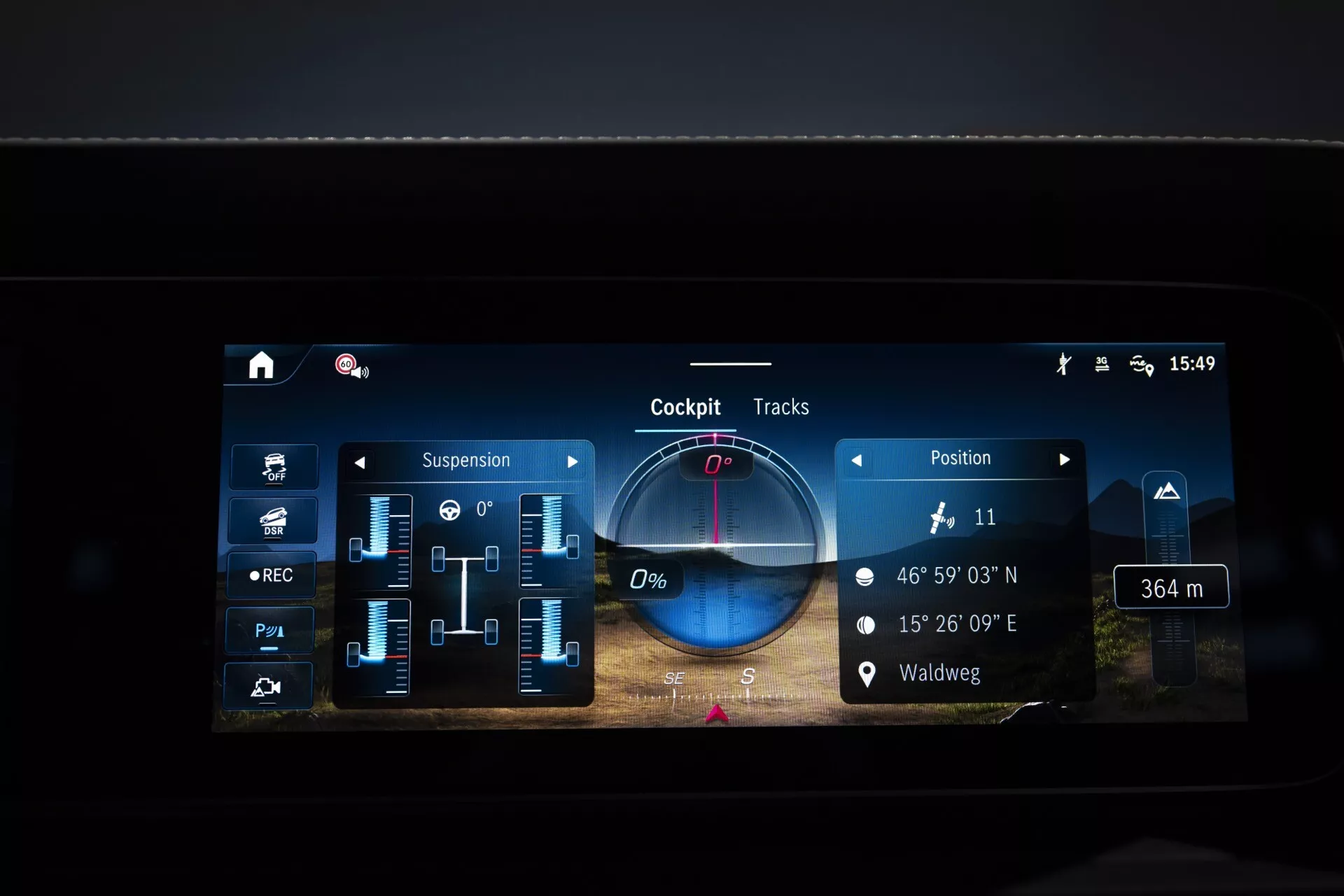 Écran d'infodivertissement de la Mercedes-Benz G-Klasse 2024 affichant les réglages de suspension, les coordonnées GPS, les informations personnalisables du cockpit et la fonctionnalité des pistes de conduite, axé sur la technologie avancée du véhicule