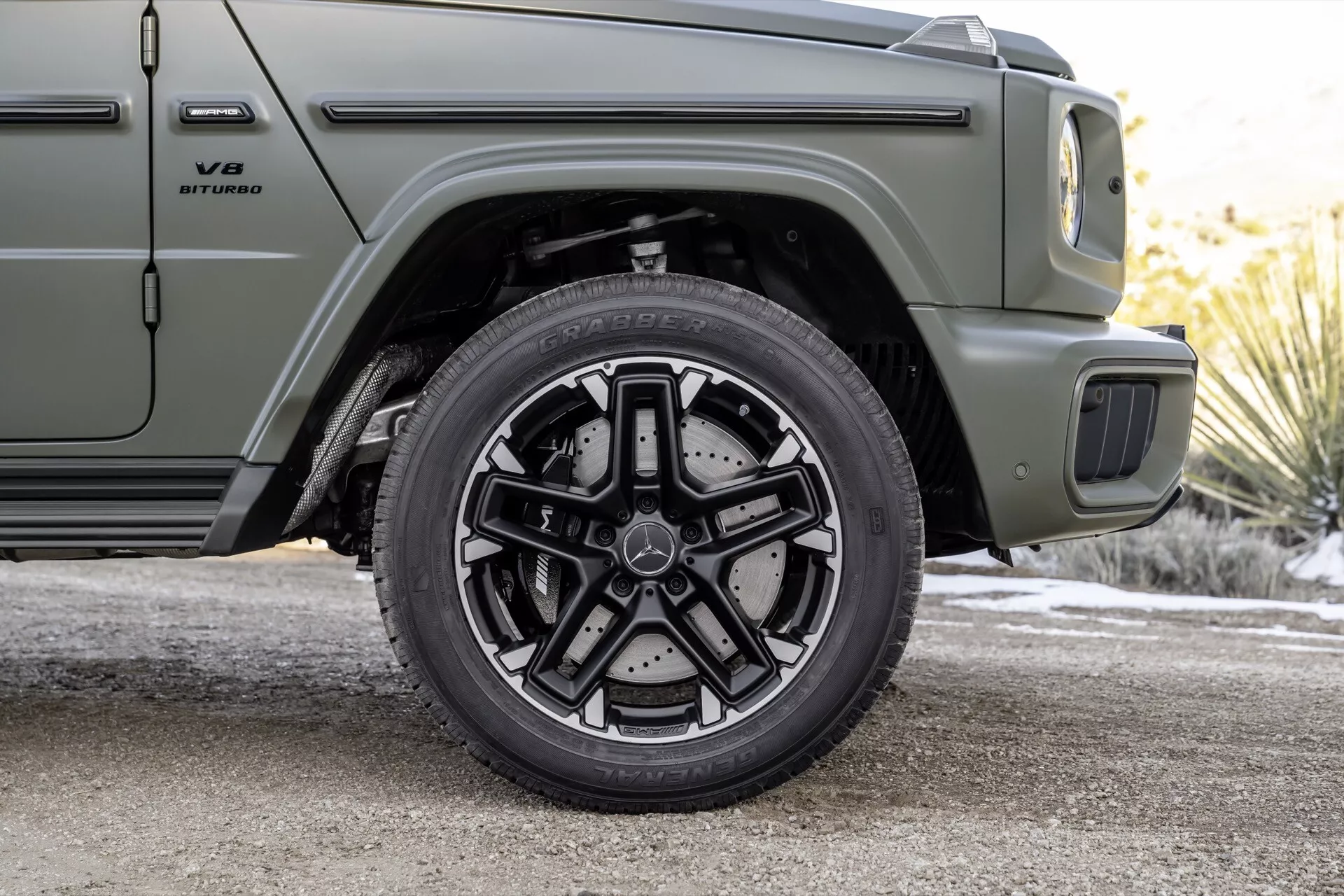 Vue rapprochée de la roue avant passager et d'une partie du profil latéral de la Mercedes-Benz G-Klasse 2024, mettant en avant le système de freinage haute performance et le design de la jante alliage à multiples branches, en vert olive mat
