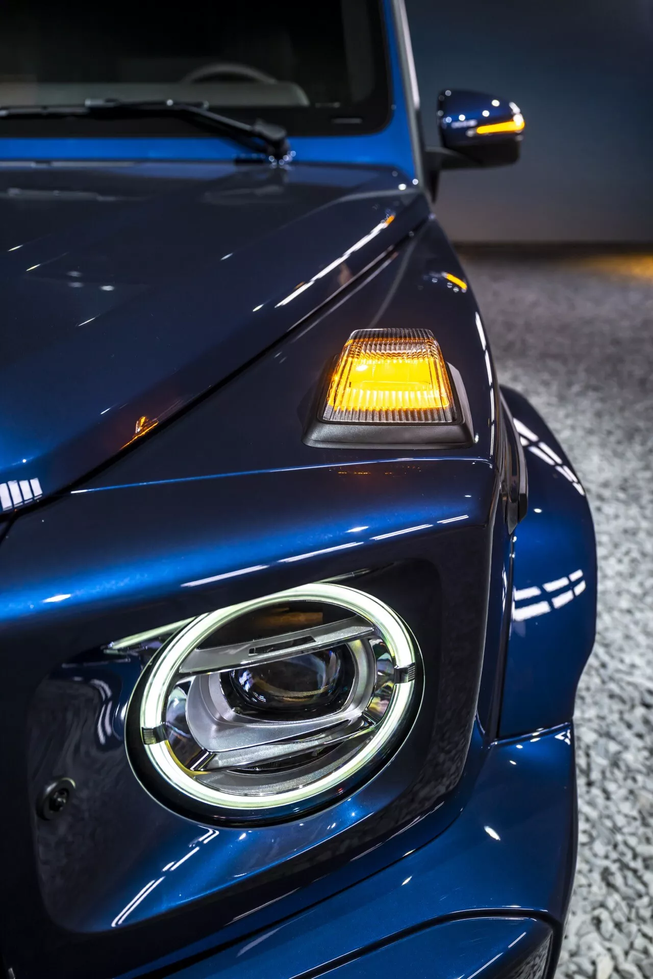Vue rapprochée du quart avant gauche de la Mercedes-Benz G-Klasse 2024, présentant la conception de phare LED, la finition premium en bleu métallique profond et les caractéristiques de sécurité avancées