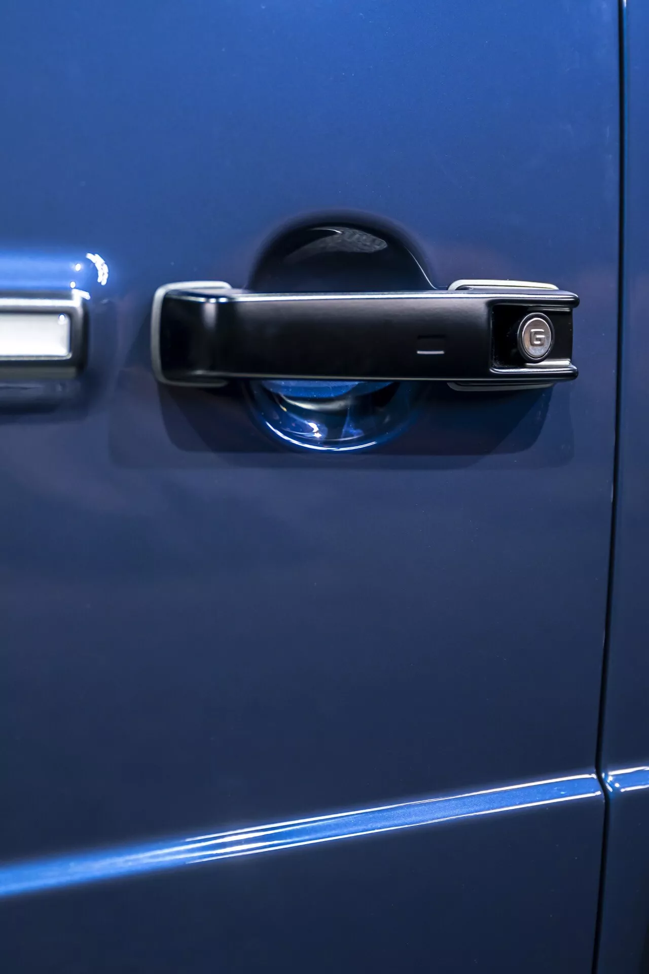 Vue en gros plan de la poignée de porte d'une Mercedes-Benz G-Klasse 2024 bleue, avec un design traditionnel comprenant un trou de serrure et un indicateur de verrouillage, prise de vue latérale avec une faible profondeur de champ