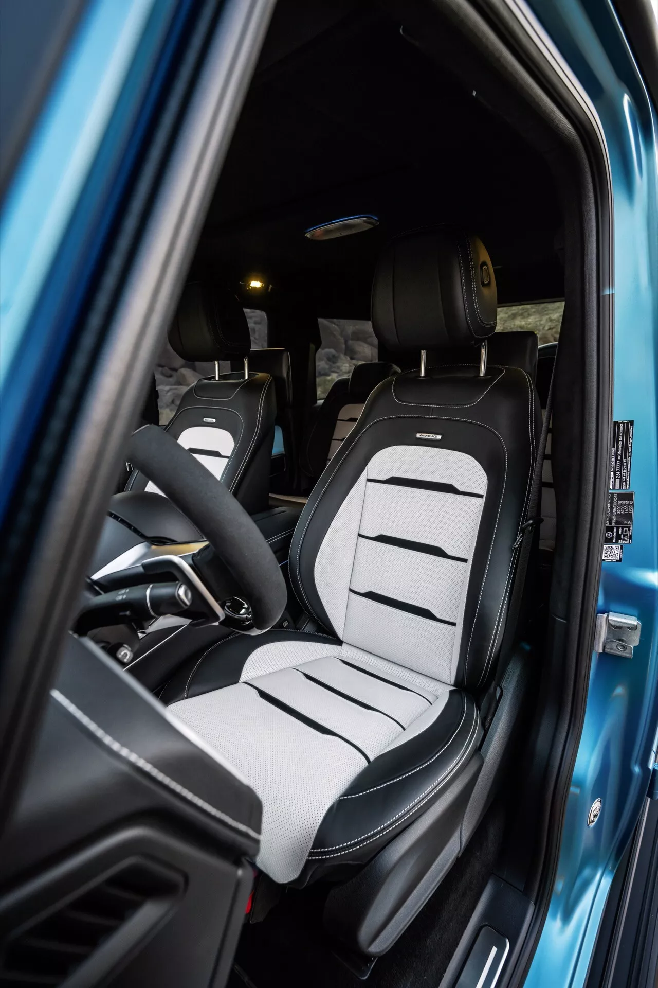 Vue intérieure de la Mercedes-Benz G-Klasse (465) 2024 mettant en avant le siège conducteur avec une sellerie bicolore et un design de siège baquet moderne à travers la porte ouverte