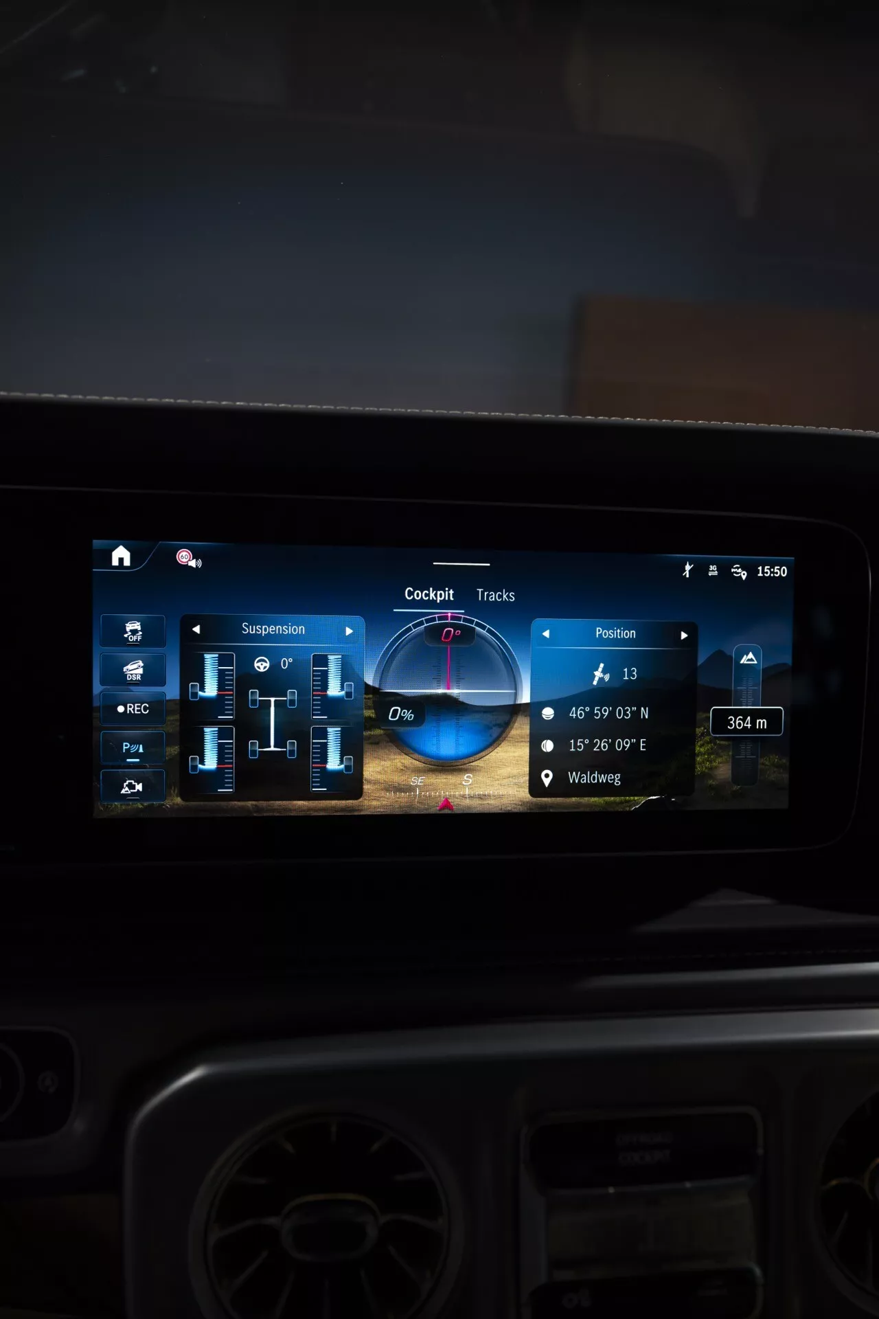 Vue rapprochée de l'écran tactile moderne du système d'infodivertissement dans une Mercedes-Benz G-Klasse 2024, présentant navigation, réglages de suspension, pistes pour le hors-route et commandes multimédias, reflétant des technologies automobiles avancées et un design intérieur de luxe.