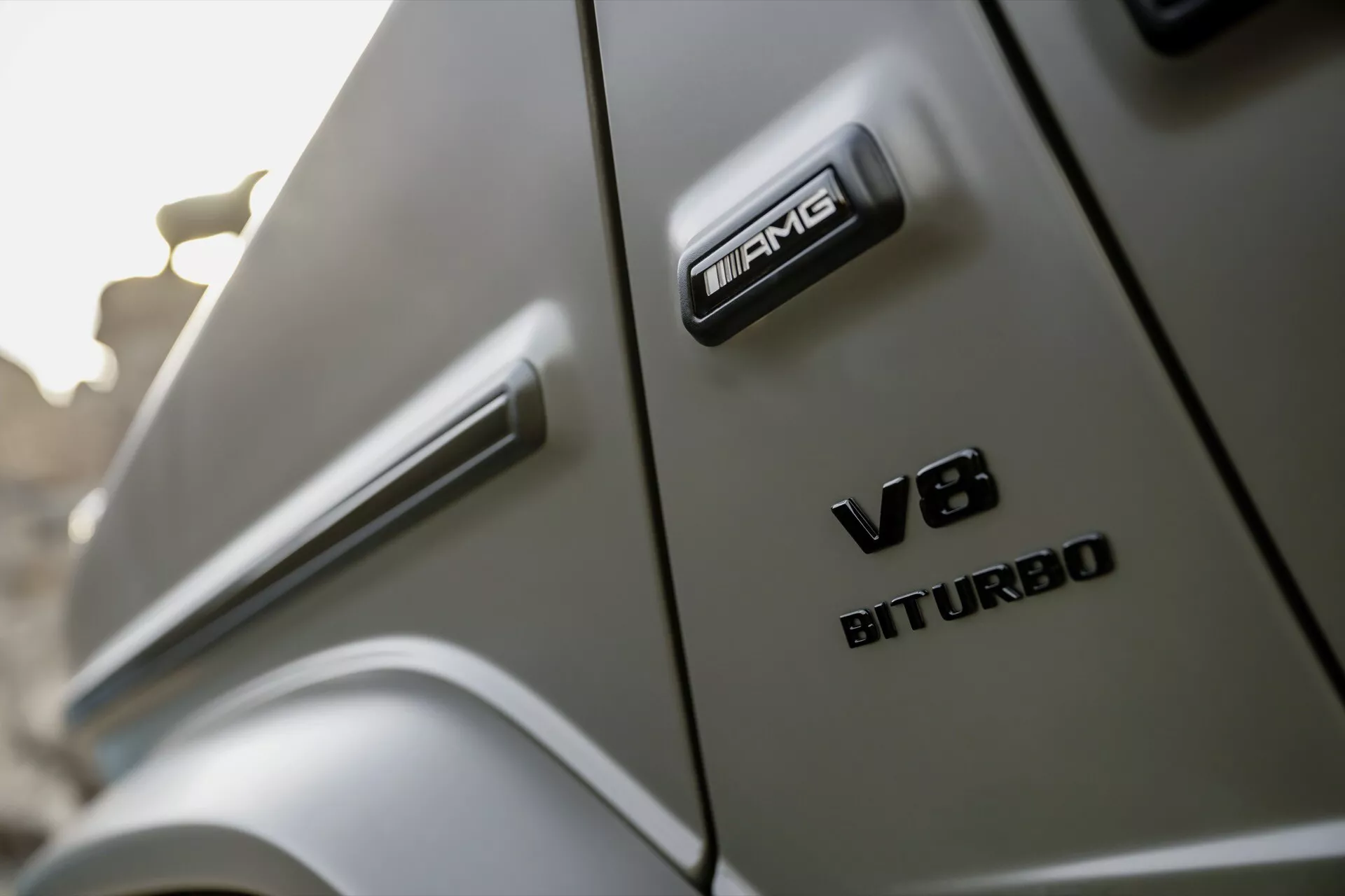 Vue rapprochée et angulaire mettant en évidence les badges AMG et V8 BITURBO sur la nouvelle Mercedes-Benz G-Klasse 2024, soulignant les éléments de design de haute performance et de luxe du véhicule.