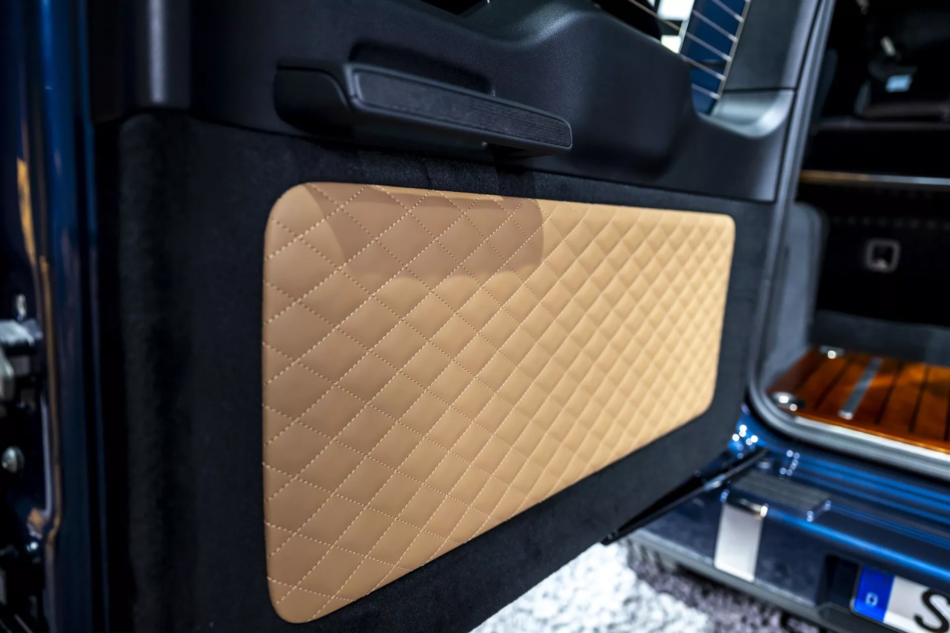 Vue rapprochée du panneau de porte intérieur de la Mercedes-Benz Classe G (G 465) 2024 avec détails en cuir beige matelassé et poignée noire, mettant en lumière l'artisanat et le design de luxe
