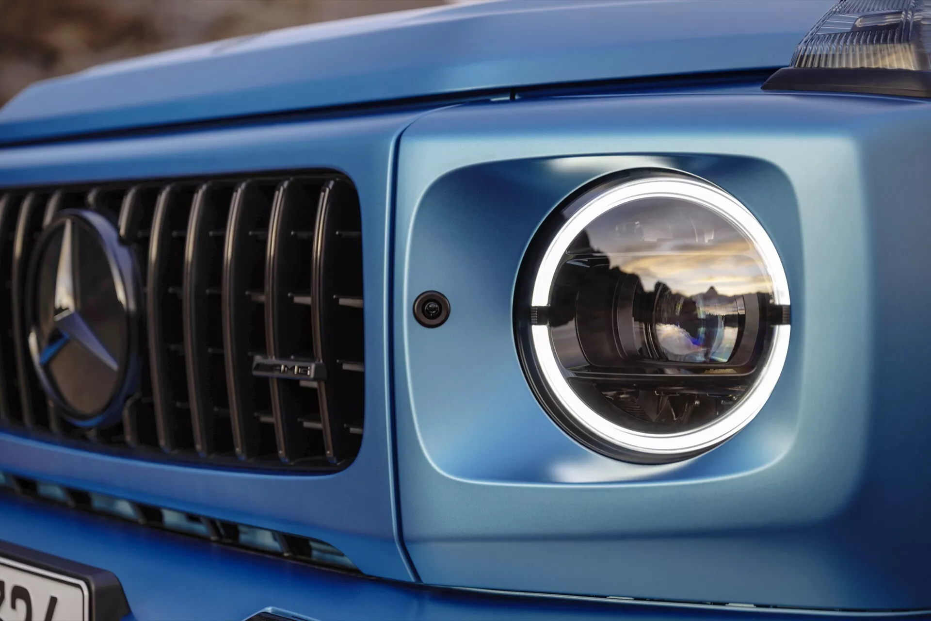 Vue rapprochée de la section avant gauche de la Mercedes-Benz Classe G 2024 mettant en évidence le phare projecteur moderne, une partie de la grille et la carrosserie bleue métallique