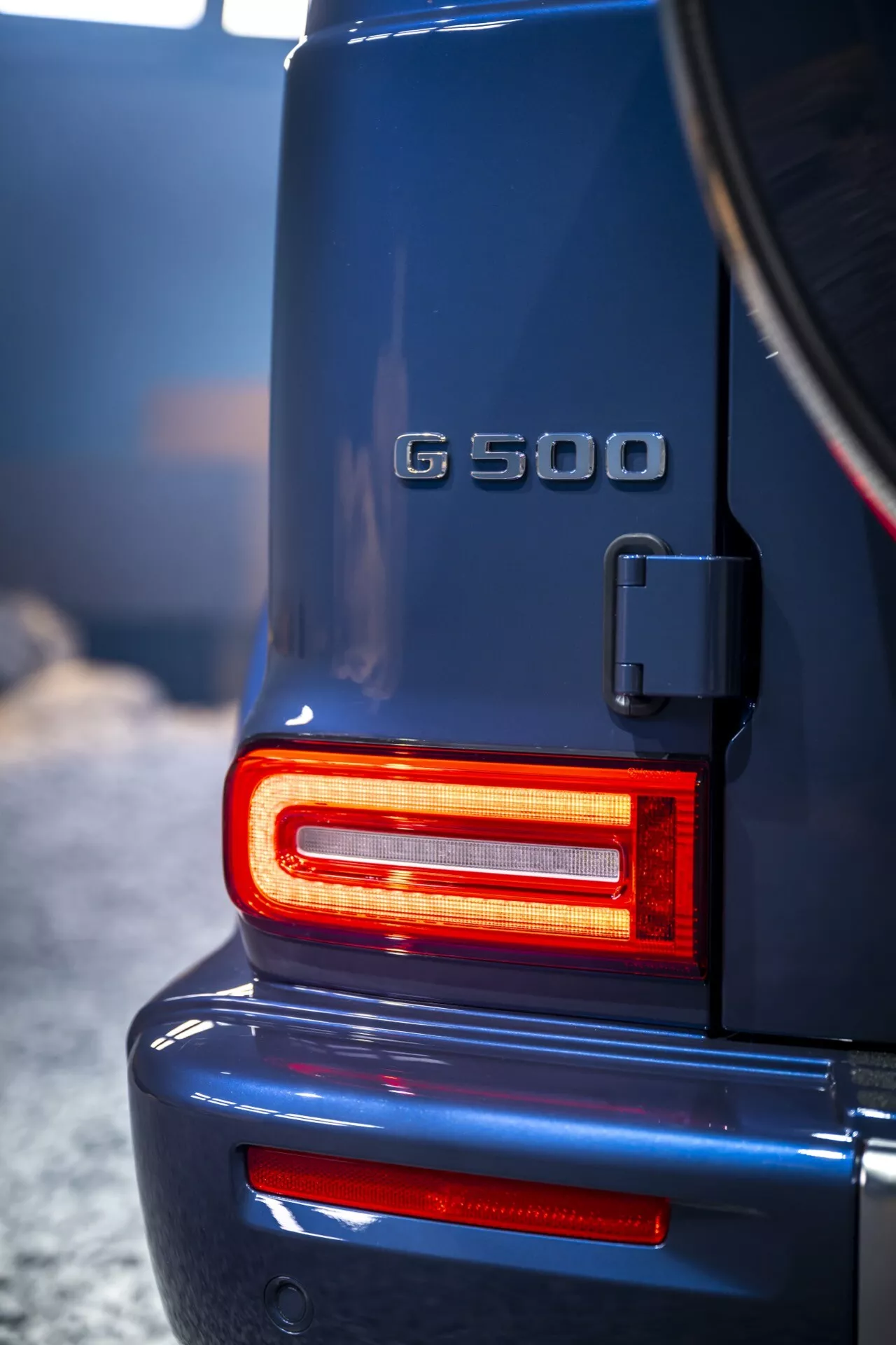 Section arrière de la Mercedes-Benz Classe G (G 500) 2024 avec feux arrière LED modernes illuminés en rouge, mettant en avant son design robuste de haute qualité et symbole de statut de SUV de luxe avec une vue claire du porte-roue de secours et de l'insigne du modèle.