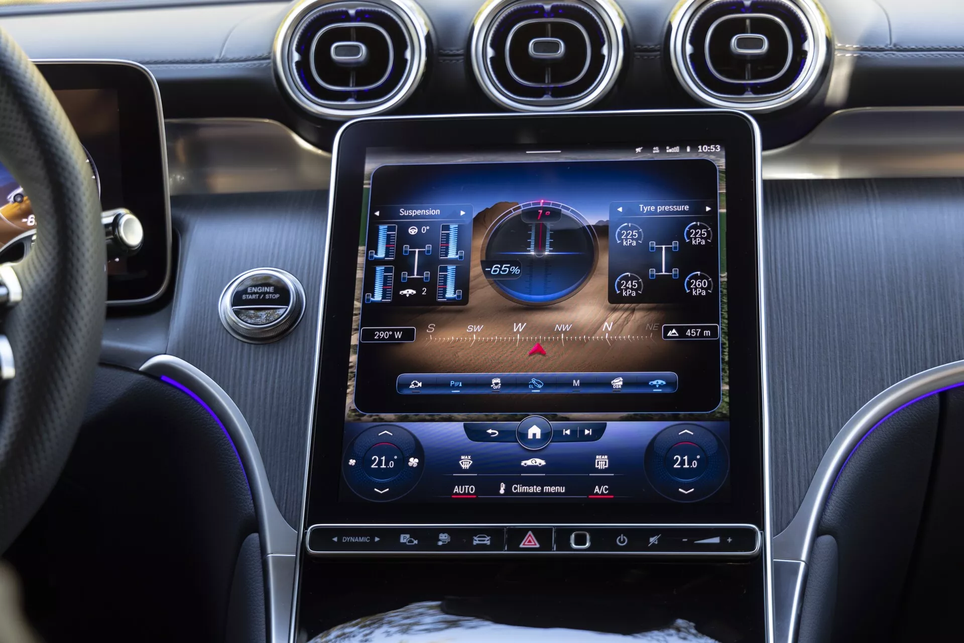 Vue intérieure d'une Mercedes GLC 2022 axée sur le système d'infodivertissement central et le tableau de bord, avec un grand écran tactile affichant des graphiques haute résolution, y compris une carte de navigation GPS, les informations sur la pression des pneus et un indicateur de conduite écologique. En dessous, des commandes de climatisation bi-zone, et au-dessus, trois bouches d'aération circulaires avec une finition métallique. L'image, prise du point de vue du passager, montre également une partie du volant et suggère des matériaux premium comme le métal brossé et le cuir à l'intérieur de l'habitacle.