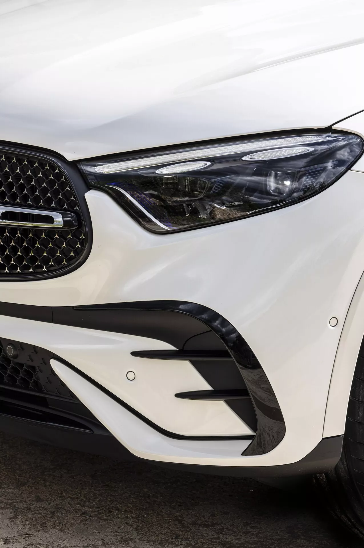 Image en gros plan de la section avant de la Mercedes GLC 2022 montrant le phare LED élégant, la calandre en nid d'abeille et les éléments angulaires du pare-chocs, capturée sous un angle oblique mettant en valeur l'éclairage avancé et le design aérodynamique.