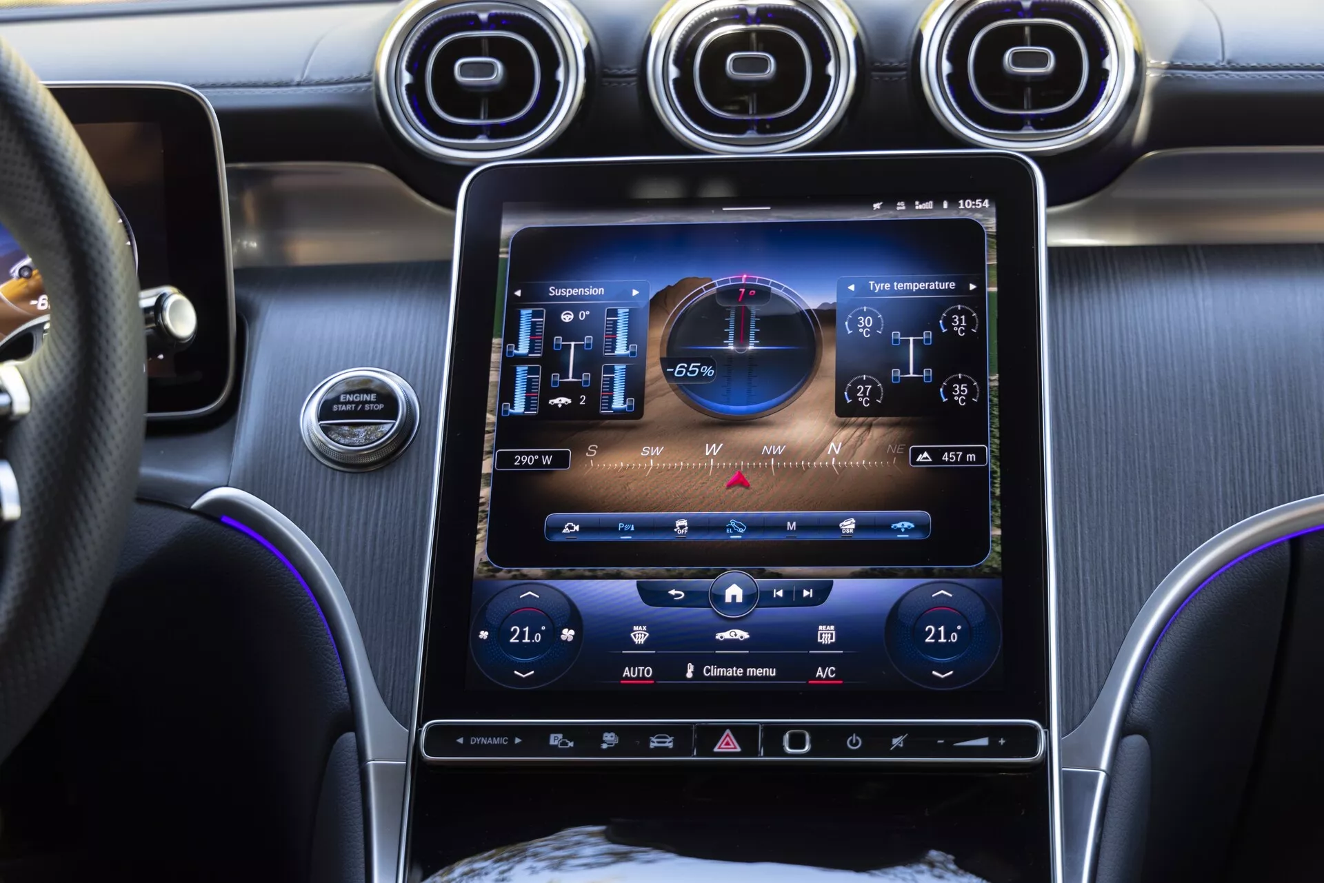 Vue rapprochée de la console centrale de la Mercedes GLC 2022 avec un système d'infodivertissement à écran tactile vertical de 10 à 12 pouces affichant l'état du véhicule avec un compteur de vitesse numérique, un compte-tours et des commandes climatiques indiquant 21 degrés Celsius pour le passager et le conducteur. L'intérieur luxueux comprend des aérateurs avec des accents chromés, un bouton de démarrage/arrêt du moteur, un volant multifonction en cuir et un éclairage d'ambiance bleu.
