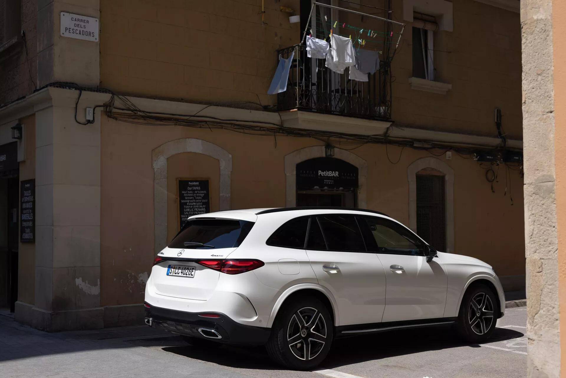 SUV de luxe contemporain garé dans une rue de la ville, capturé sous un angle arrière trois-quarts, montrant des feux arrière LED élégants, un double échappement et un hayon arrière. Le profil latéral met en évidence des jantes distinctives de grande taille, des roues sportives, des rétroviseurs latéraux redessinés avec des indicateurs de direction potentiels, un toit ouvrant et une peinture solide propre, soulignant les caractéristiques modernes et de performance dans un environnement urbain.