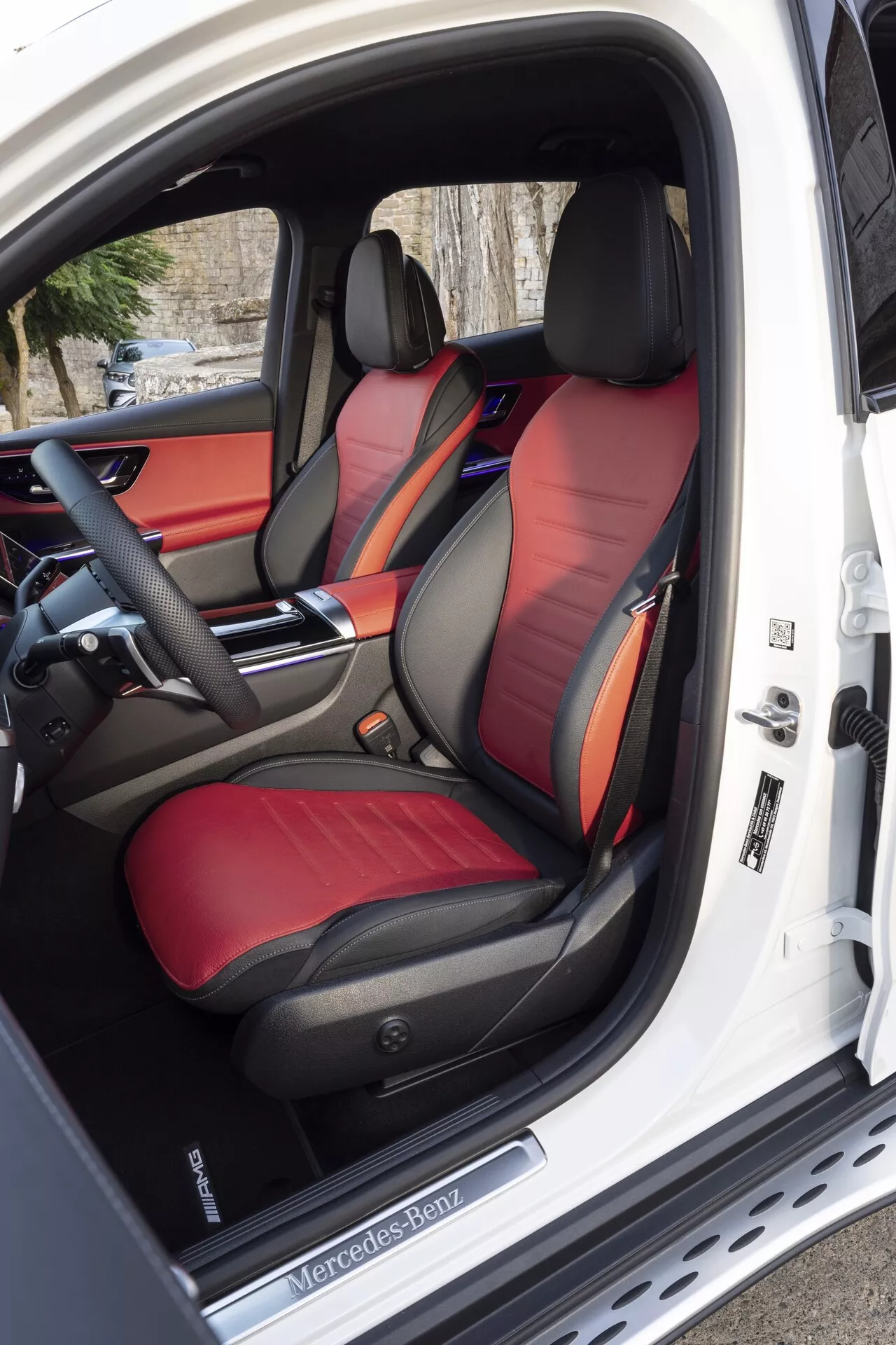 Vue intérieure du Mercedes-Benz GLC 2022, mettant en évidence les sièges avant sport bicolores en cuir lumineux, le panneau de contrôle avancé des sièges sur la porte du côté conducteur ouverte, et un volant multifonction avancé et un tableau de bord élégant partiellement visibles avec un éclairage d'ambiance personnalisable.