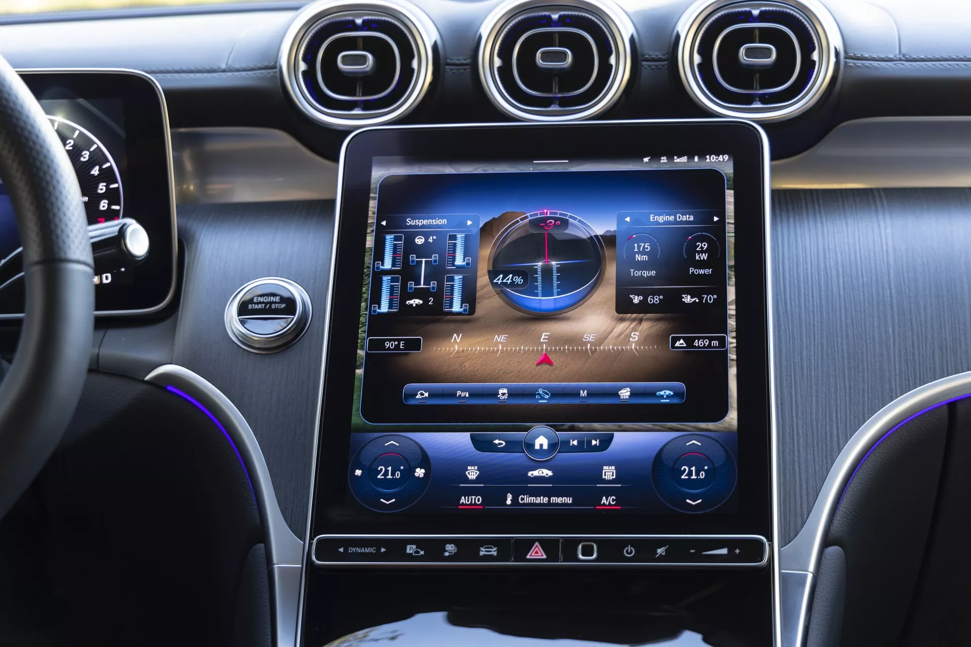 Vue au niveau des yeux depuis le siège passager avant de l'intérieur d'une Mercedes GLC 2022, mettant en évidence la console centrale avec un grand système d'infodivertissement à écran tactile vertical affichant GPS, audio et commandes de climatisation. Trois aérateurs circulaires métalliques au-dessus de l'écran, aperçu du tableau de bord et du volant à gauche, avec un éclairage d'ambiance violet accentuant la console et le tableau de bord.