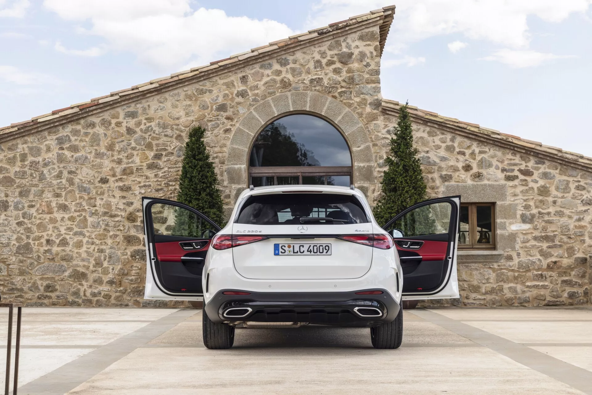 Vue arrière d'une Mercedes GLC 2022 à l'arrêt avec le coffre ouvert et les portes arrière entrebâillées, mettant en avant un système d'échappement double, des feux arrière LED élégants, une plaque d'immatriculation montée, un badge de modèle et un plancher de chargement plat pratique avec des panneaux de porte intérieure arrière au schéma de couleurs contrastant et des garnitures métalliques.