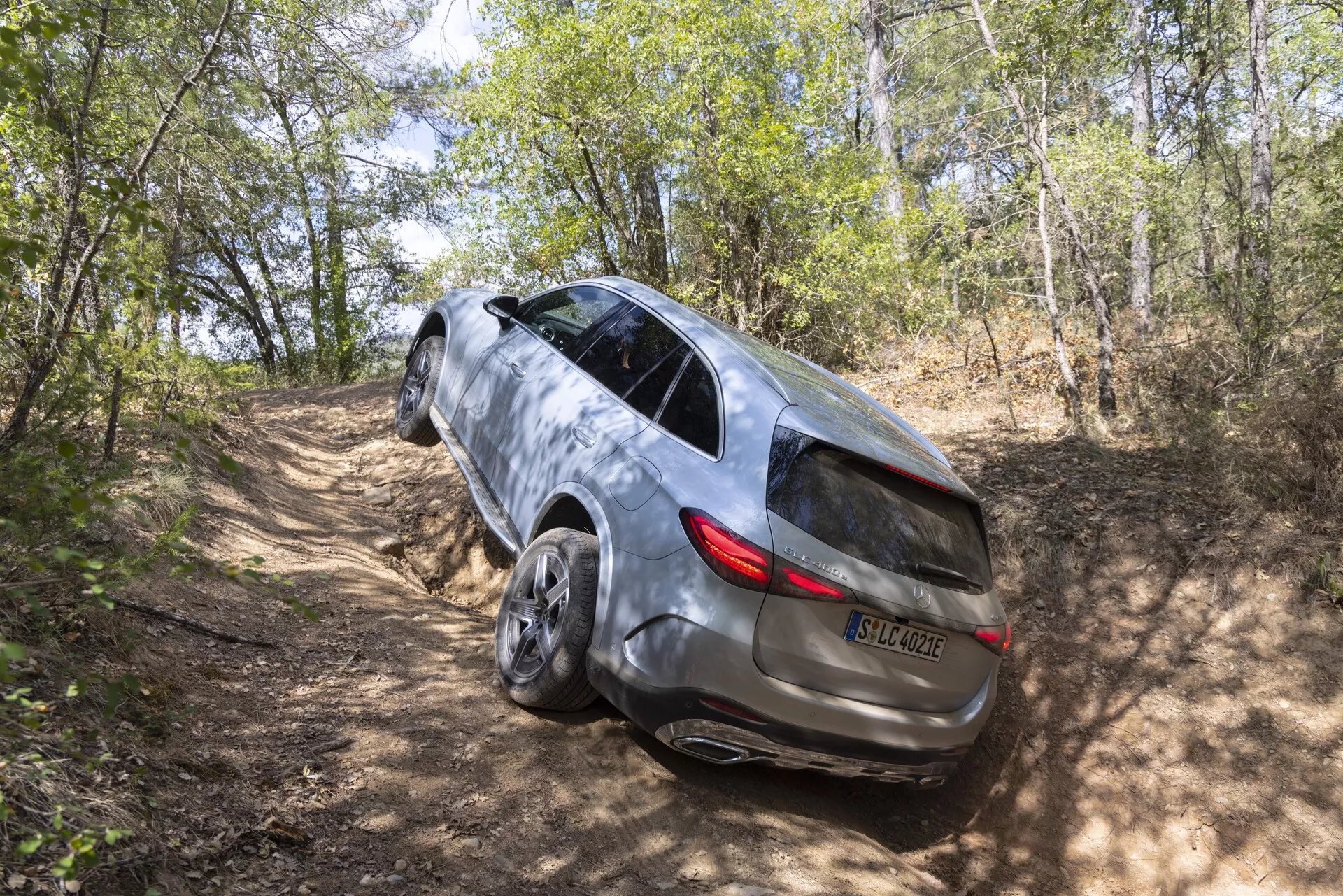 Vue arrière en trois quarts d'un SUV Mercedes GLC 2022 sur un sentier de terre dans une zone boisée, montrant sa capacité à quatre roues motrices, son design élégant avec toit panoramique, ses feux arrière à LED, sa finition en peinture métallique, ses vitres latérales teintées avec clignotants intégrés, poignées de porte encastrées et grandes roues en alliage.