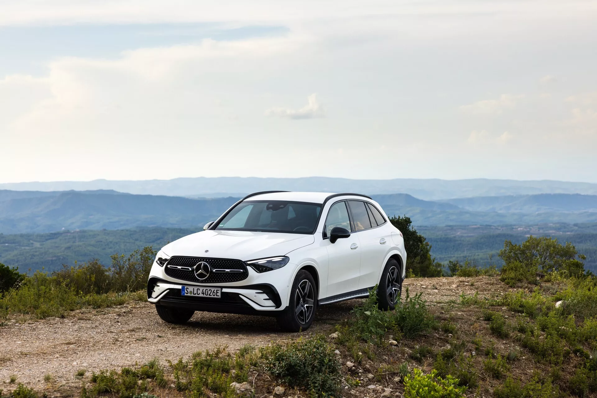 Profil latéral du Mercedes GLC 2022 blanc sur un chemin de terre accidenté, mettant en évidence la tenue de route, la garde au sol et les lignes de conception du SUV. Les caractéristiques visibles comprennent la calandre avant et le badge de marque, les phares à LED, les jantes en alliage, les rétroviseurs latéraux avec clignotants intégrés, les lignes aérodynamiques de la carrosserie, la finition de peinture brillante et le motif de la bande de roulement. L'éclairage naturel de jour améliore les caractéristiques esthétiques et fonctionnelles de la voiture.
