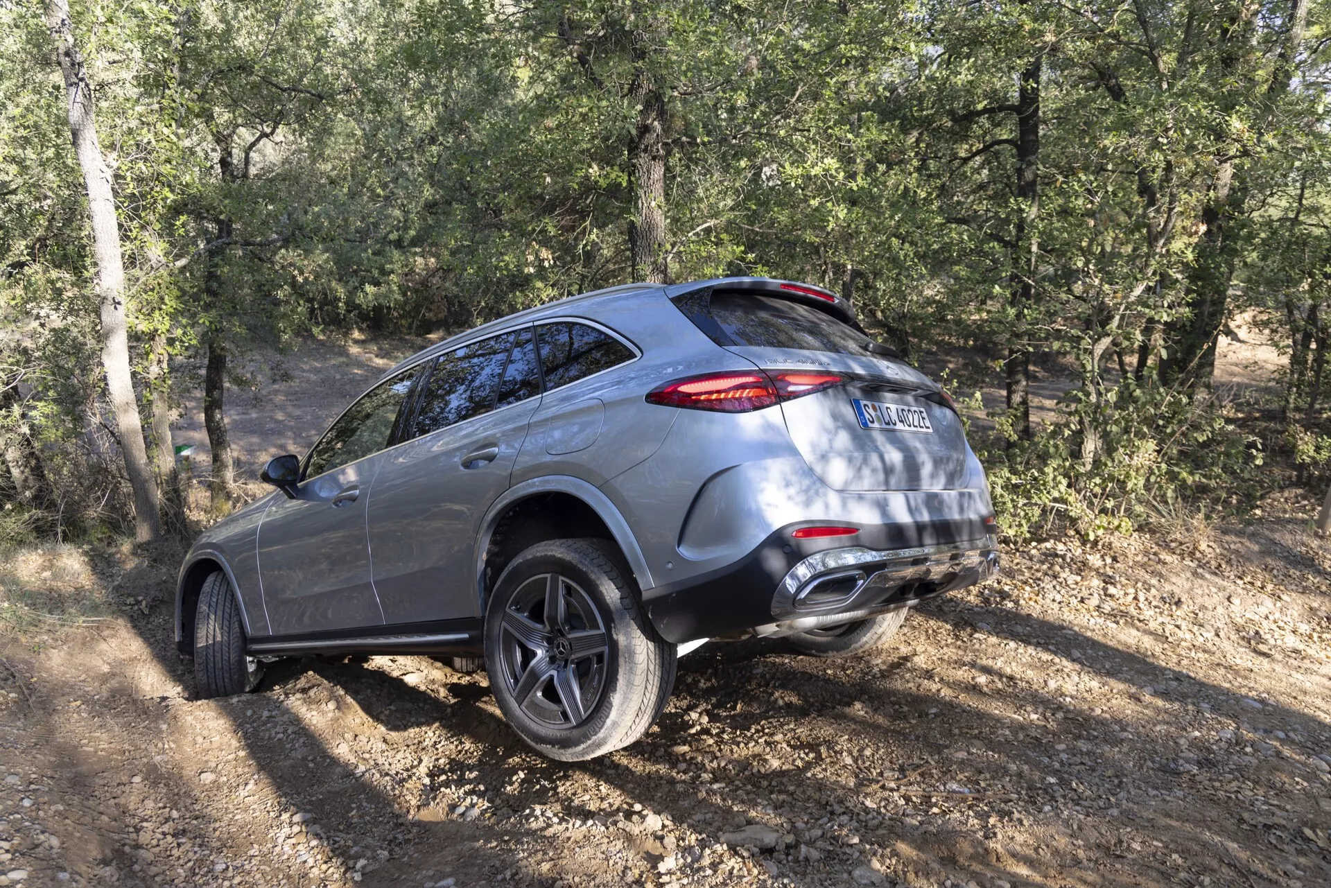 Vue de trois quarts arrière d'un SUV Mercedes GLC 2022 sur terrain non pavé, montrant ses caractéristiques de luxe et de design moderne telles que des roues en alliage à plusieurs rayons, des feux arrière à LED, un système d'échappement double et des capacités tout-terrain avec un fond de feuillage et d'arbres.