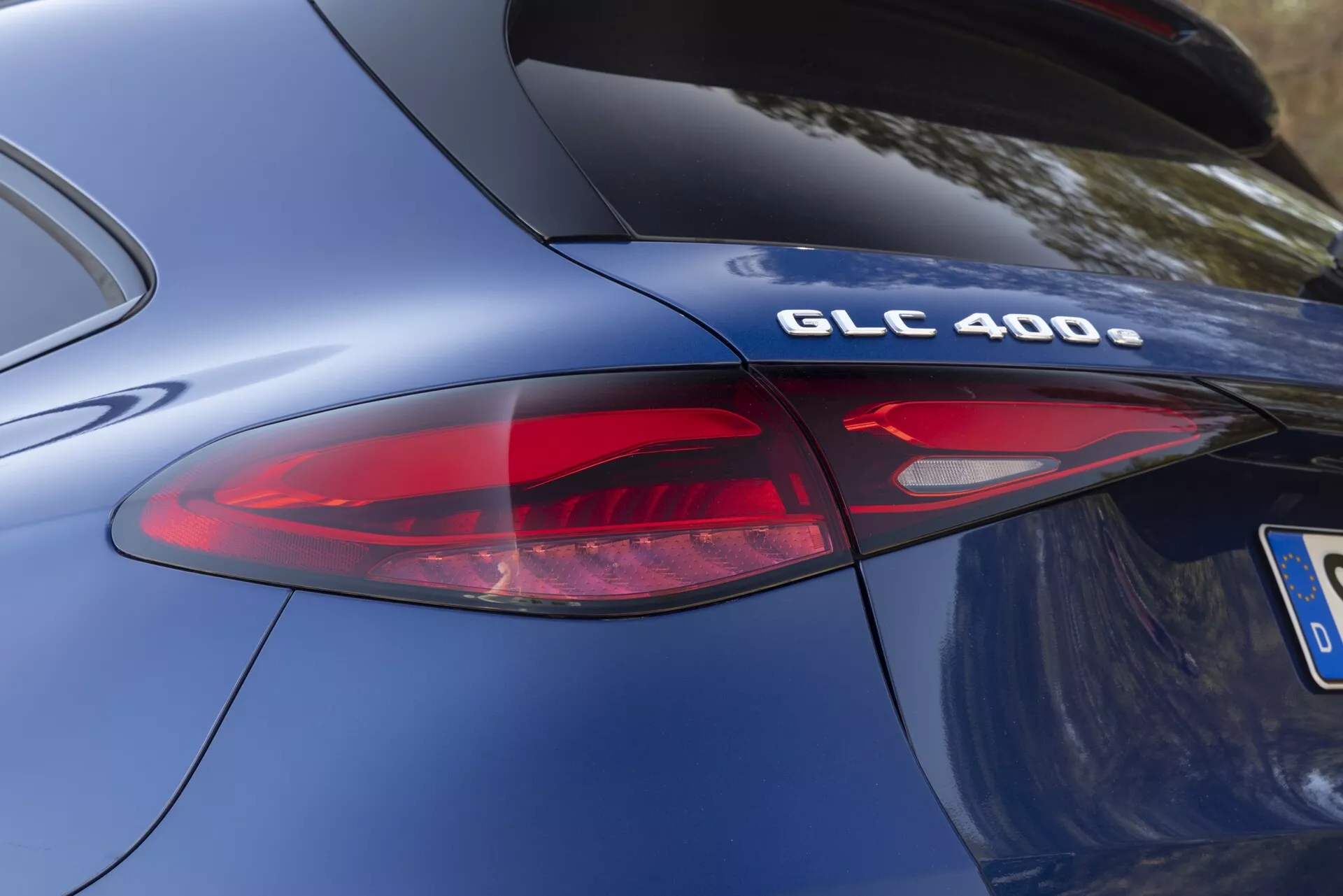 Vue rapprochée et angulée de la section arrière d'une Mercedes-Benz GLC 400 modèle 2022. L'accent est mis sur la désignation du modèle 'GLC 400' et une partie de l'ensemble de feux arrière à LED modernes. La photo met en évidence la courbure de la carrosserie de la voiture, la peinture métallique bleue lisse et le design élégant des éléments arrière, y compris les éléments de lentille rouges et clairs du feu arrière. La finition chromée sur le badge 'GLC 400' suggère des spécifications technologiques de performance et de chaîne cinématique.