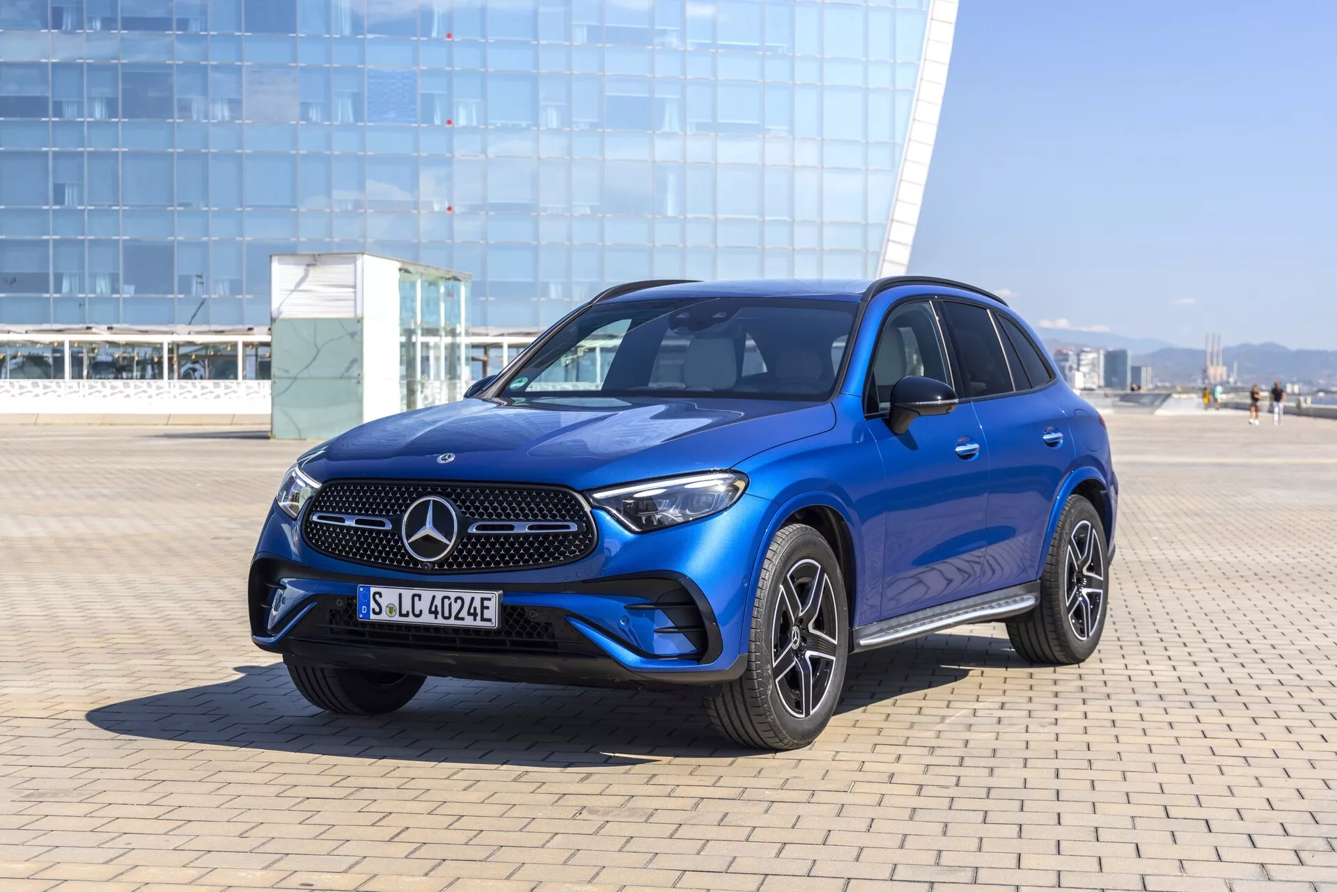 Vue trois-quarts avant d'un SUV Mercedes-Benz GLC 2022 bleu montrant la grille distinctive Mercedes avec l'emblème, des lamelles horizontales élégantes, un pare-chocs intégré avec phares antibrouillard et prises d'air, des phares à LED affûtés, des lignes moulées sur le capot, des jantes en alliage sport à plusieurs branches, des poignées et rétroviseurs couleur carrosserie, des vitres teintées, un toit ouvrant et des systèmes avancés d'assistance à la conduite possibles. Photographie prise dans un environnement extérieur lumineux avec lumière du jour naturelle et ciel clair.