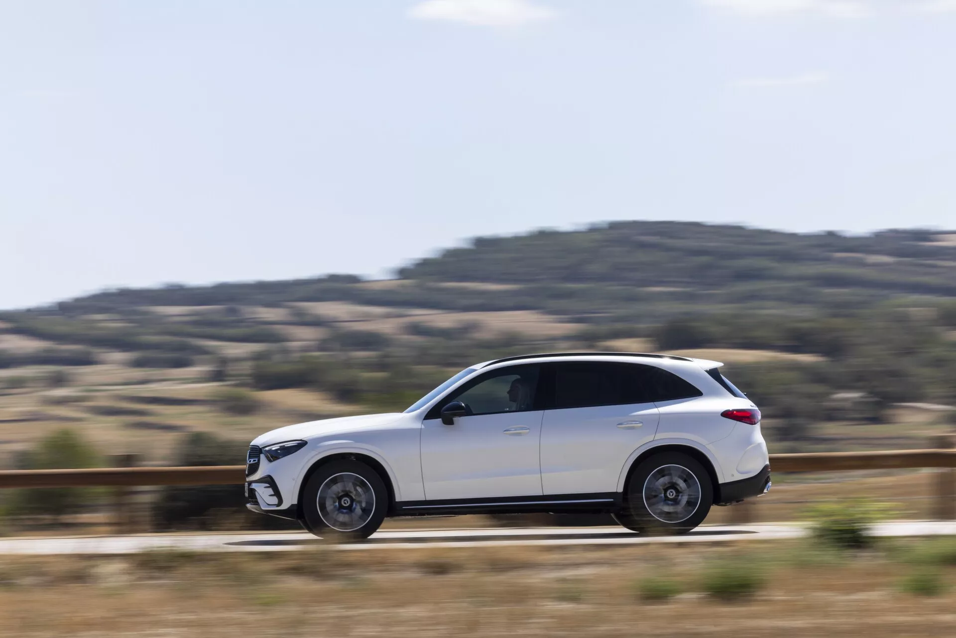Vue de profil latéral d'un SUV Mercedes GLC 2022 blanc en mouvement, mettant en avant des lignes de design élégantes, une carrosserie élégante avec des vitres teintées, des roues en alliage partiellement floues, des rétroviseurs latéraux, des poignées de porte affleurantes, des barres de toit et un angle de caméra bien équilibré avec une technique de panoramique qui met en évidence le mouvement dynamique du véhicule.