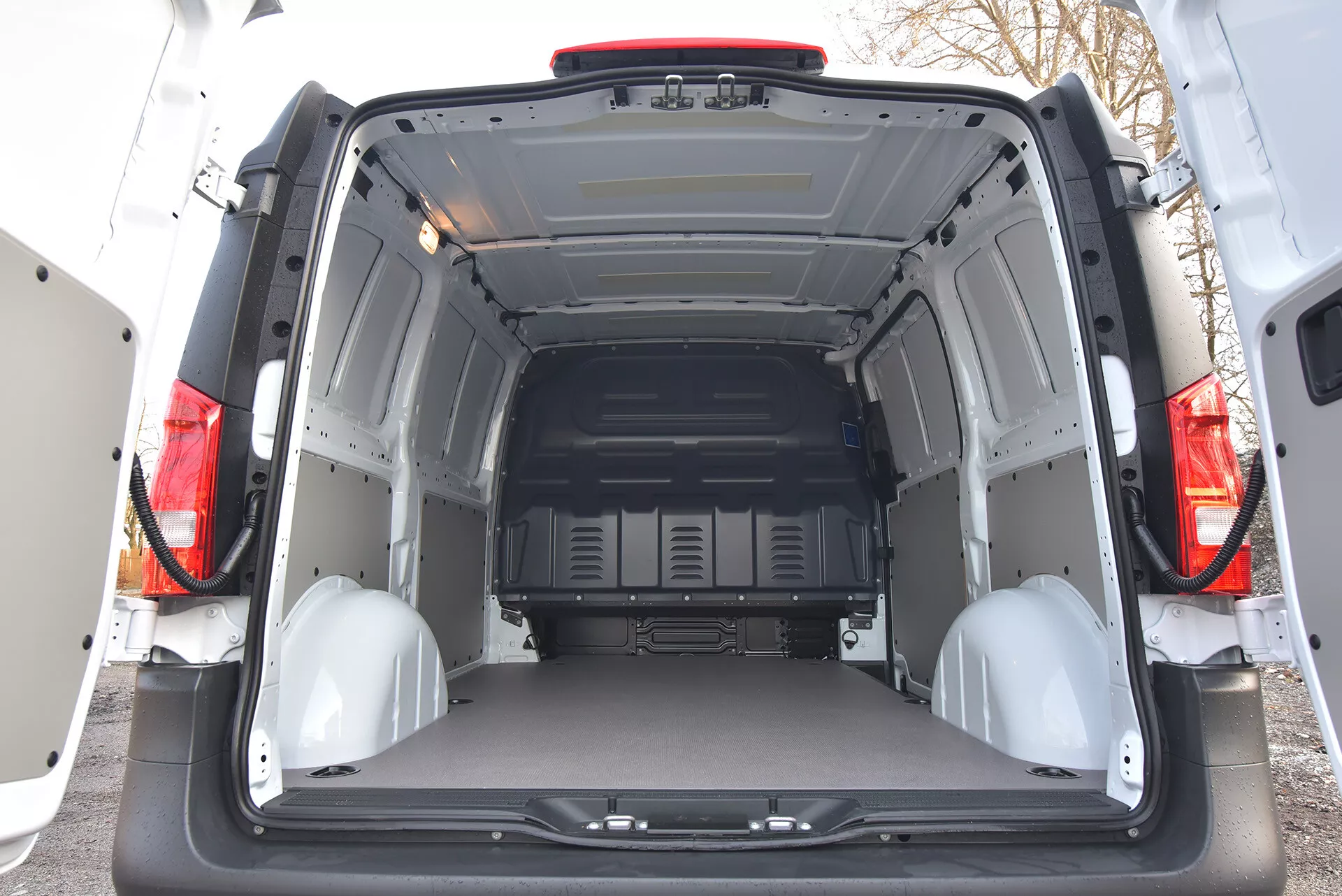 Vue intérieure arrière d'un Mercedes-Benz Vito Tourer 2014 montrant un espace de chargement spacieux et vide avec portes ouvertes, panneaux de protection et points d'arrimage