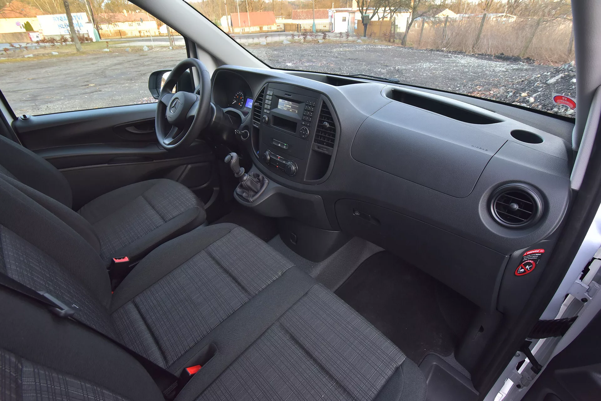 Vue intérieure du Mercedes-Benz Vito Tourer de 2014 côté conducteur montrant le tableau de bord avant, la boîte de vitesses manuelle, les panneaux de commande et les sièges en tissu