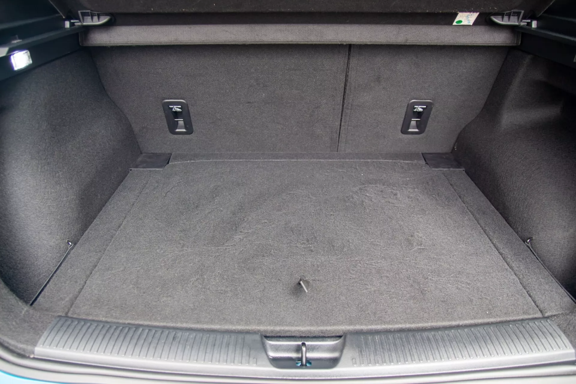 Vue directe sur le compartiment à bagages vide et moquetté d'une MG MG4 2022, montrant des crochets de chargement, des dossiers de siège arrière rabattables et un rebord protecteur