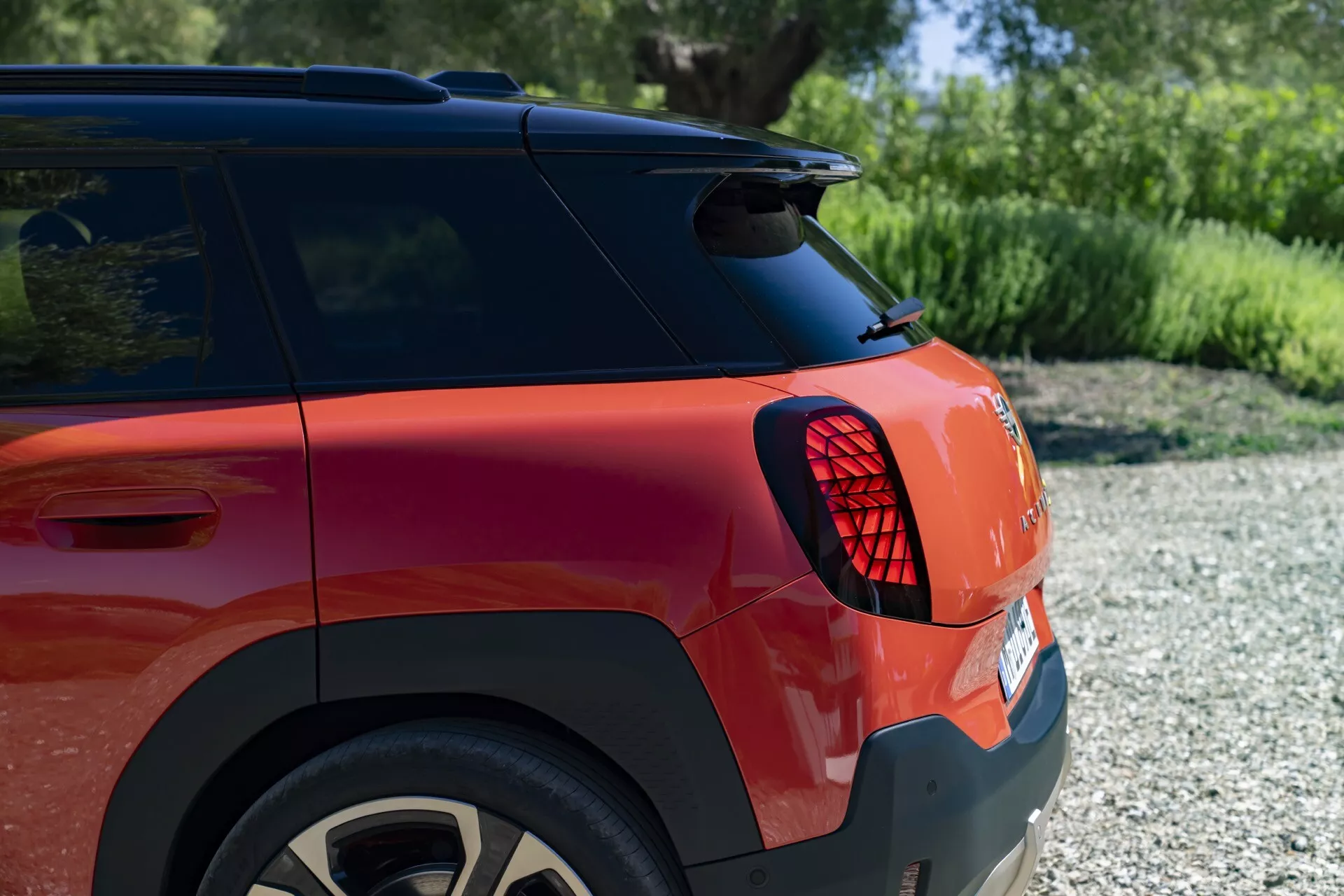 Vue rapprochée de la section arrière du MINI Aceman (J05) 2024 avec feu arrière LED, peinture métallique rouge et roue en alliage, dans un cadre naturel extérieur